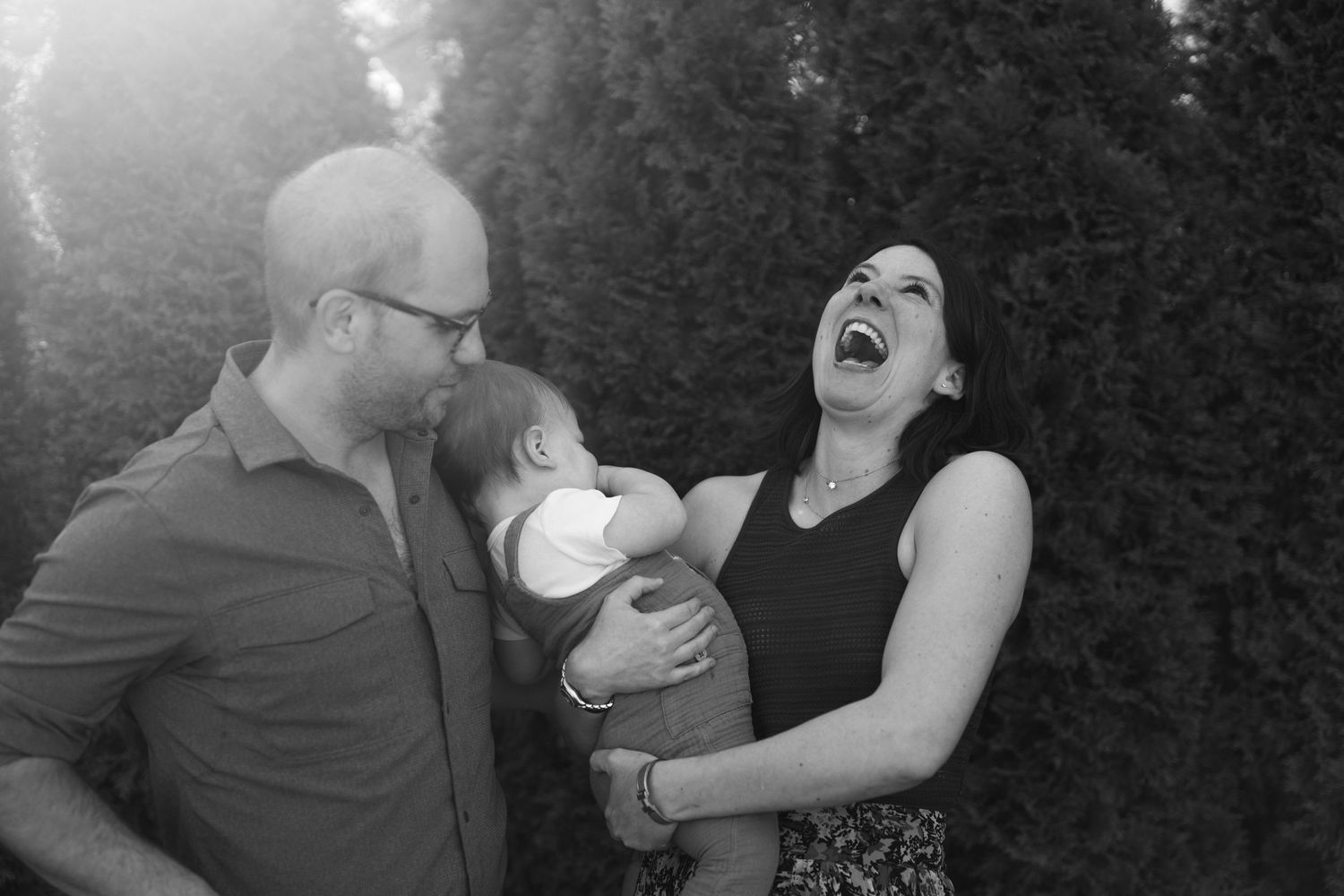 A family shares a joyful moment of laughter together outdoors in black and white photography. Mom is belly laughing
