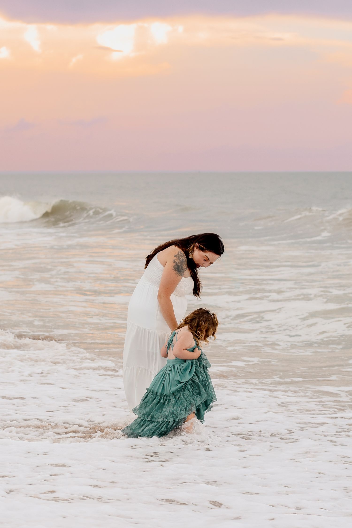 Two people walking in shallow ocean waves during sunset.