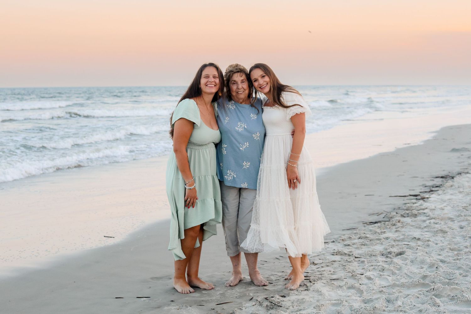 A group in coordinated blue and white outfits poses together on a sandy beach at sunset.