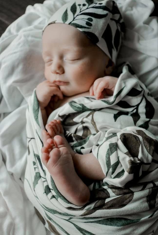 Baby sleeps wrapped in floral print swaddle blanket on white bedding.