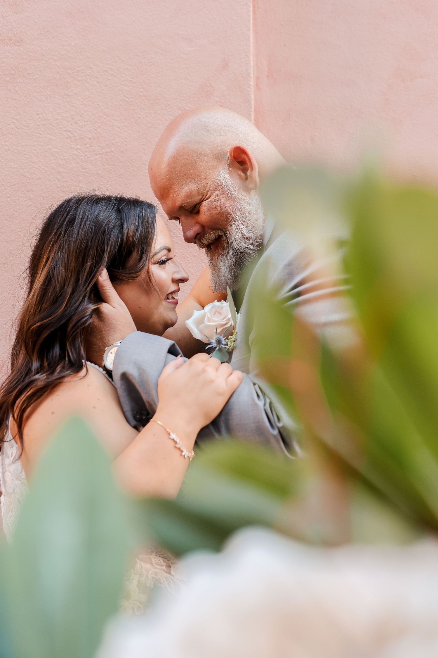 Romantic candid moments captured against a blush pink wall with greenery.