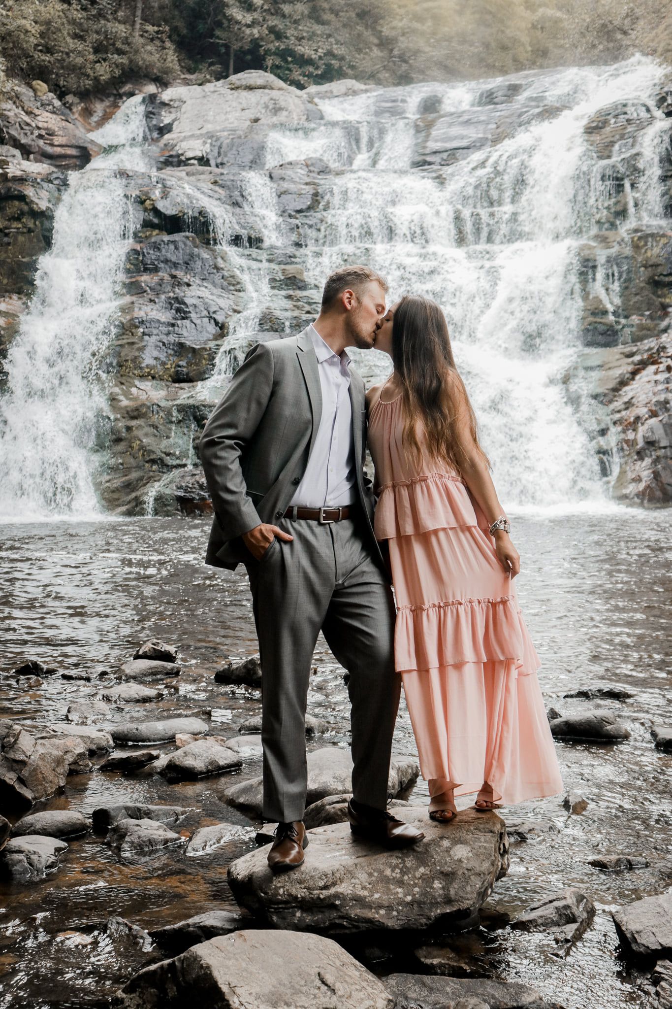 Couple sharing romantic moment in front of majestic waterfall during engagement photography session.