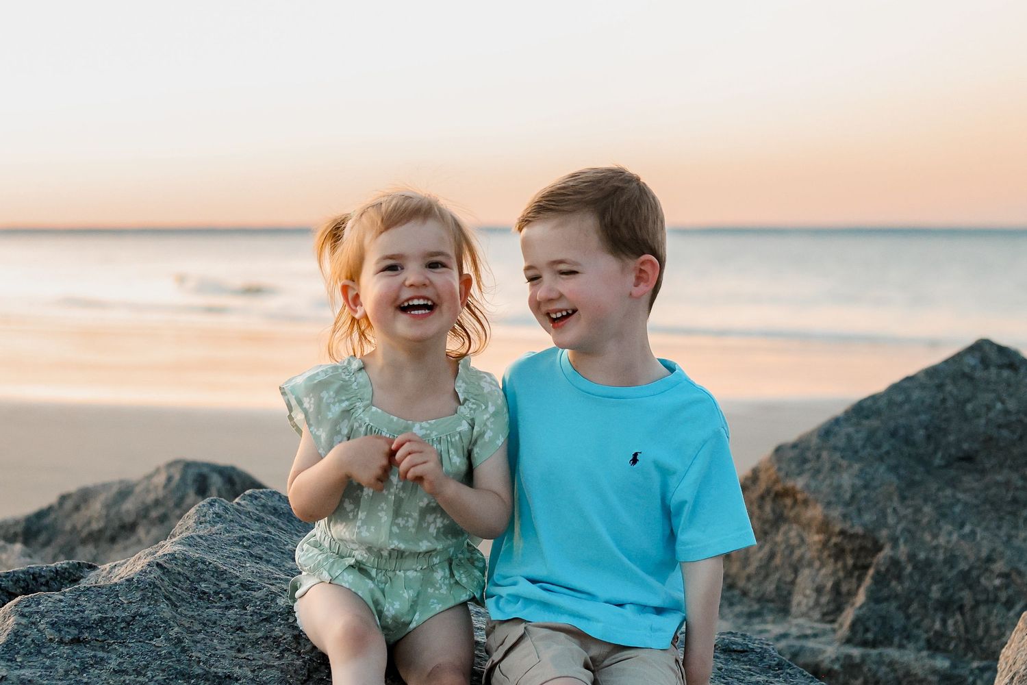 Two children sharing a laugh while sitting together during a beach photo session.