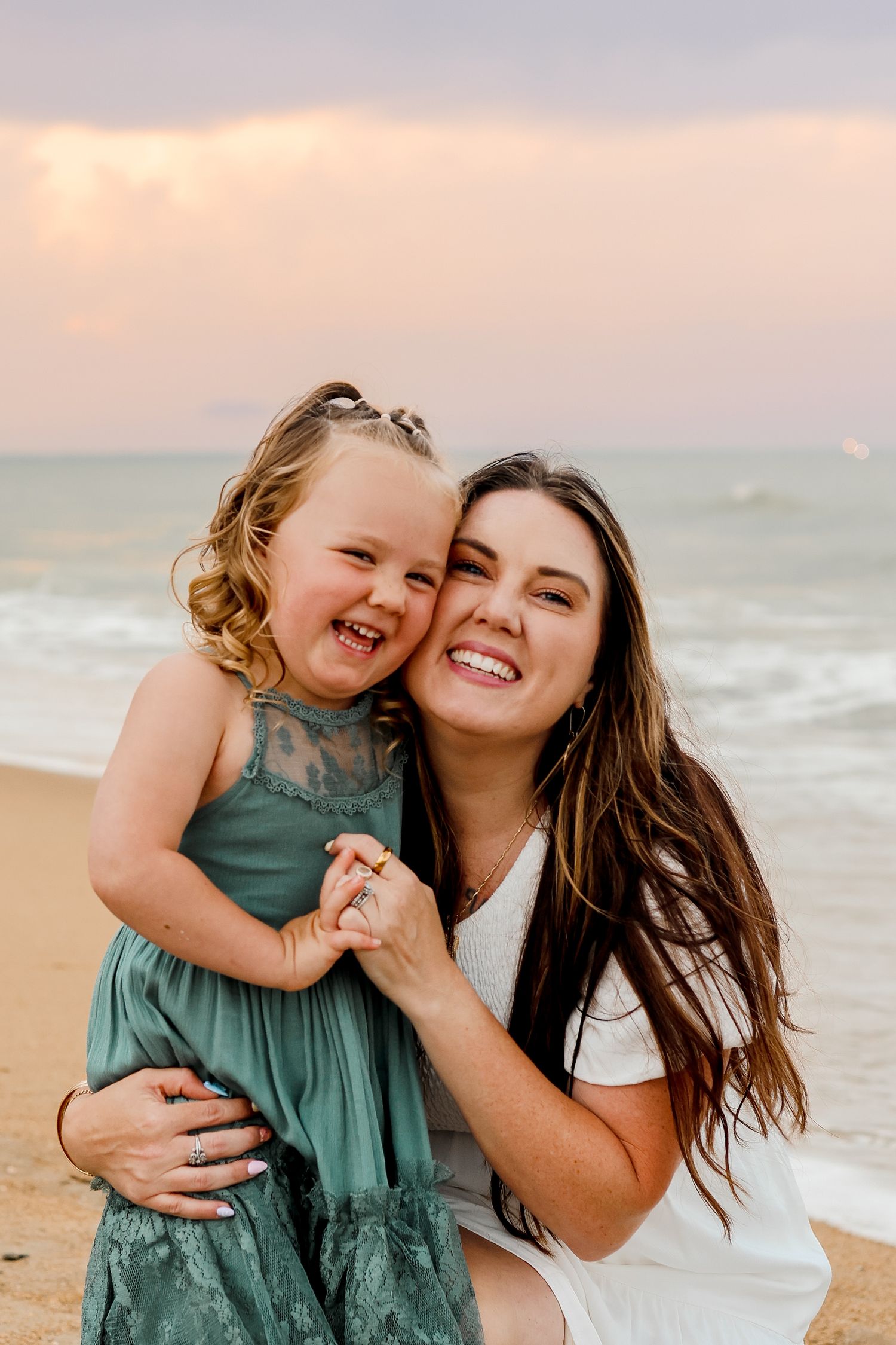 A joyful moment at sunset on the beach showing laughter and connection in matching teal dresses.