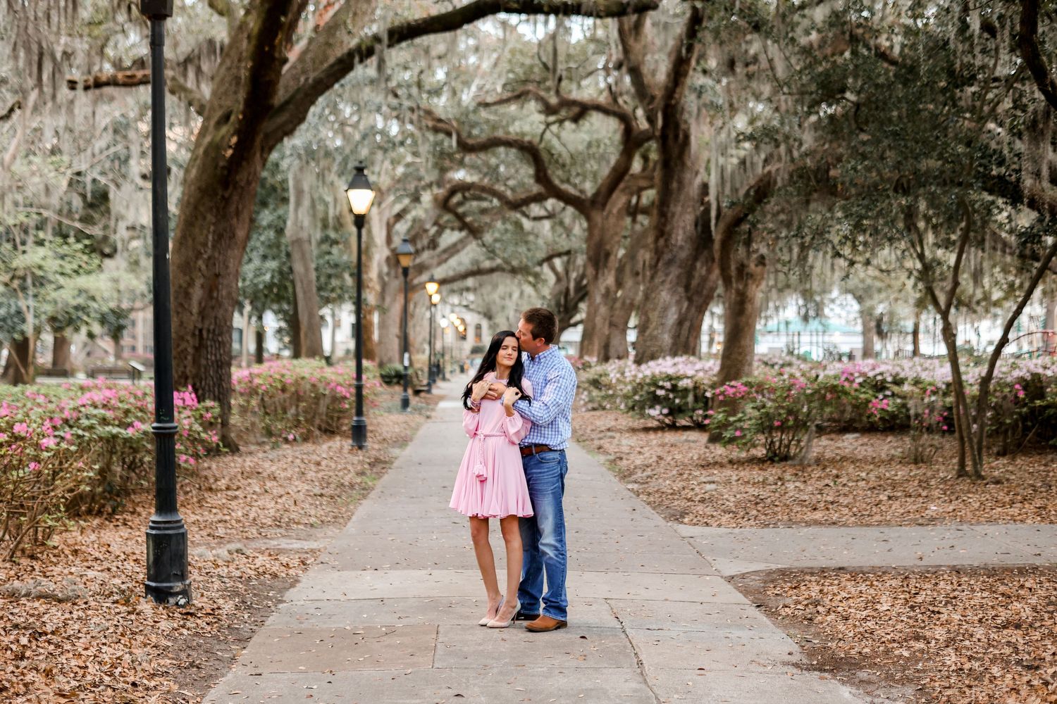 Couple walking together under Spanish moss covered trees on brick pathway.