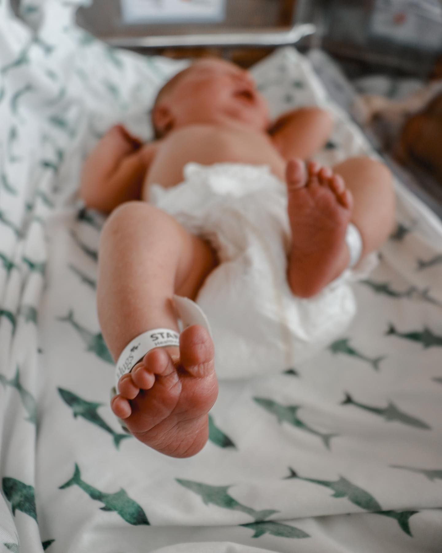 Newborn baby feet rest on patterned fabric with whale prints.
