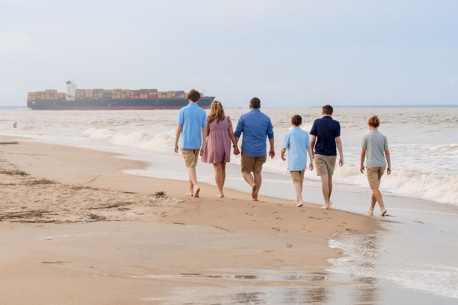 A group of people walking along the shoreline during sunset.