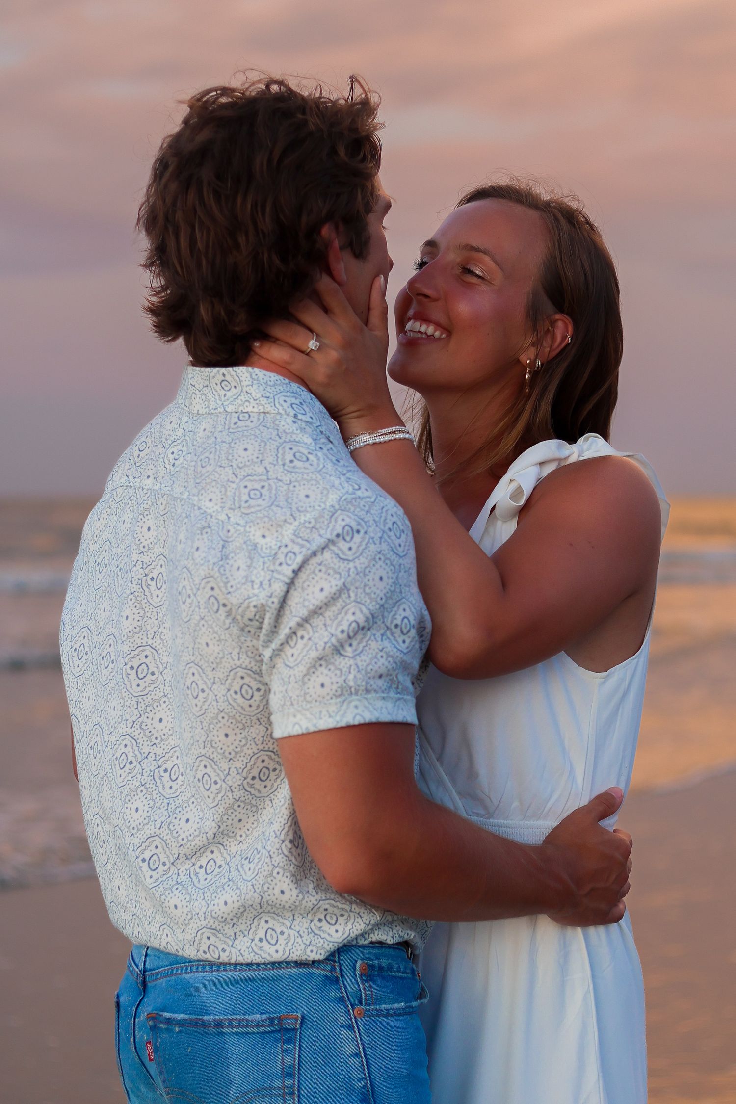 Couple sharing a tender moment while embracing on the beach at dusk.