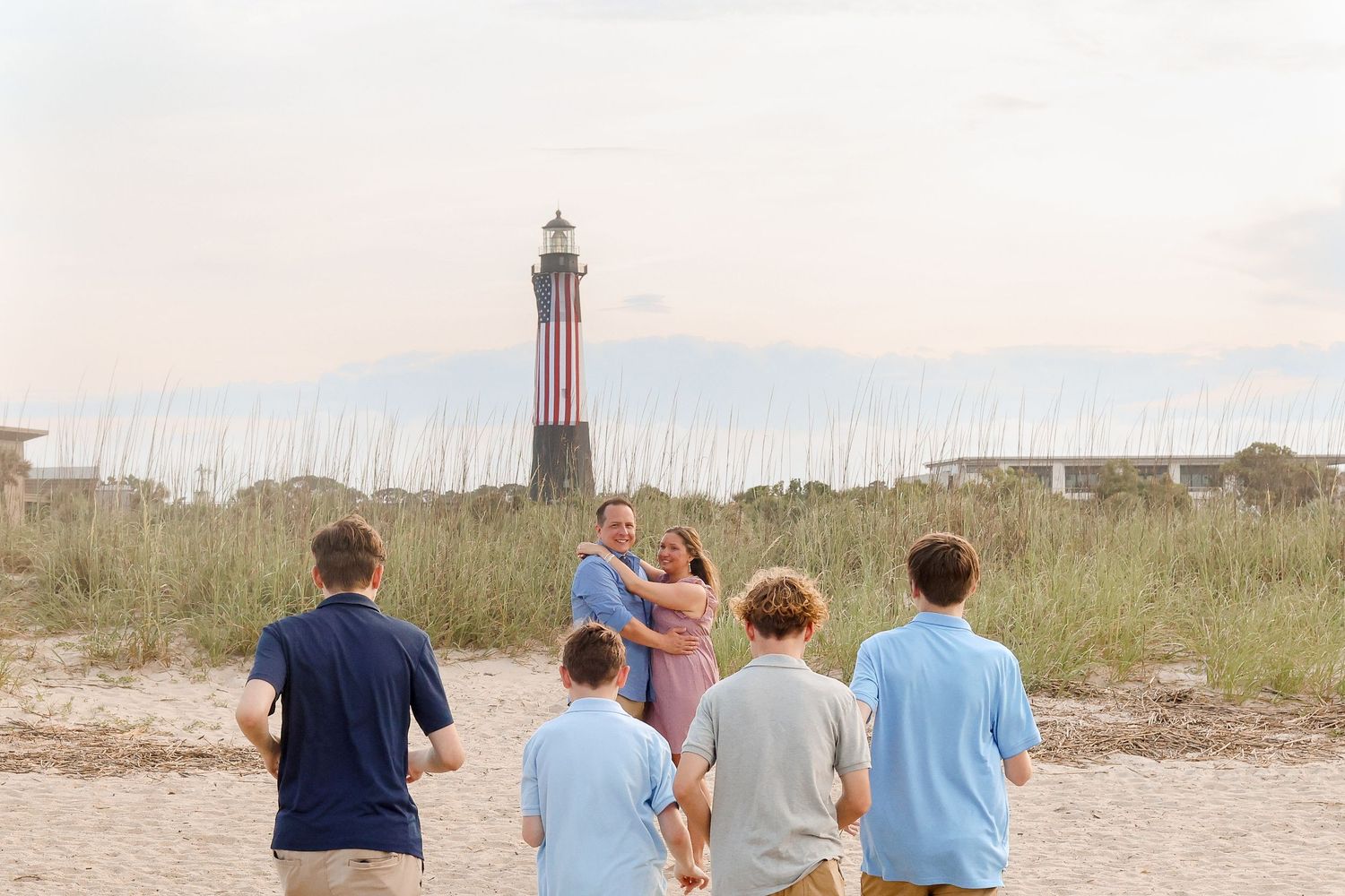 Group of people looking at a tall lighthouse among beach grass at dusk.