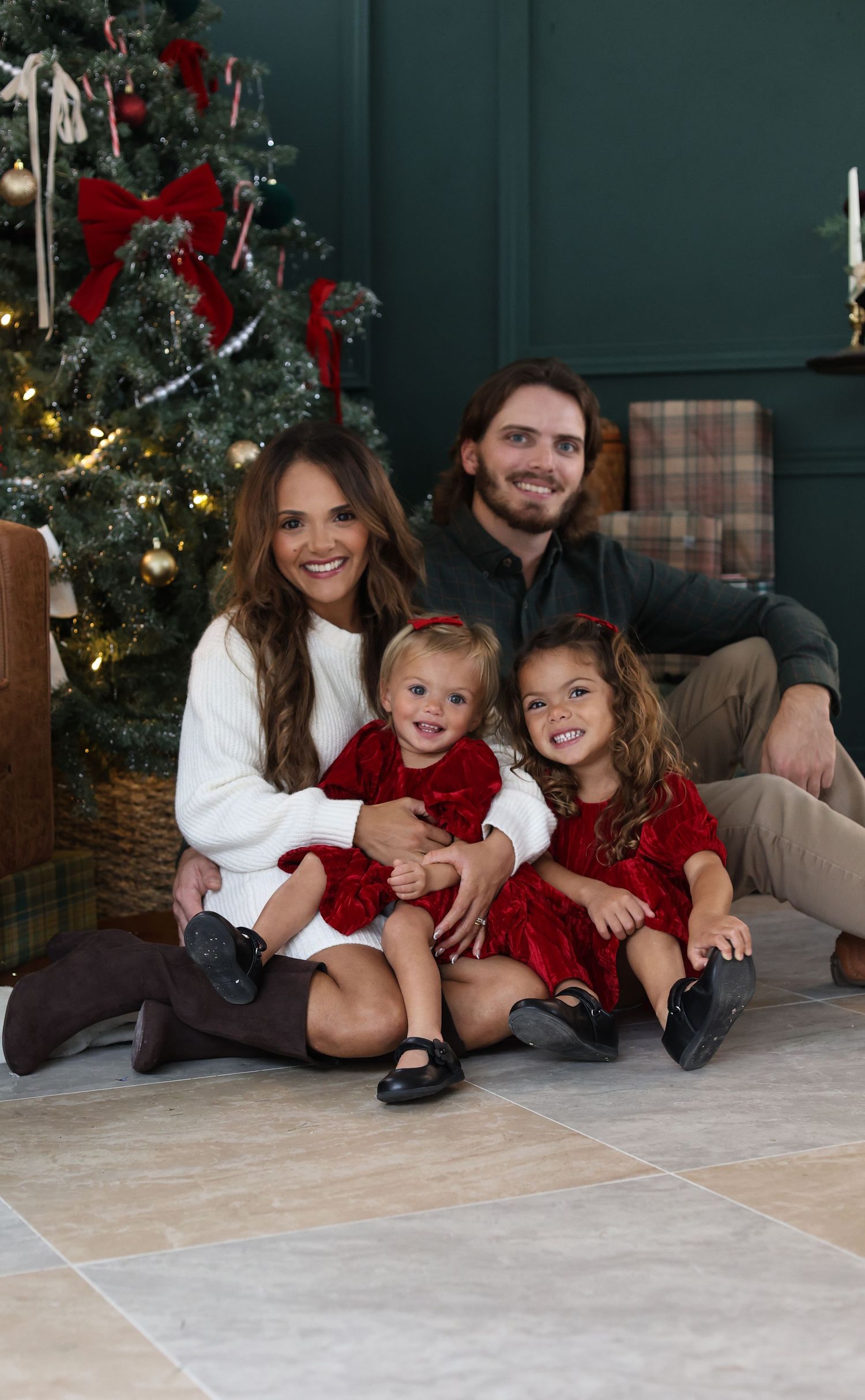 Family poses together by Christmas tree wearing coordinated red and white holiday outfits.