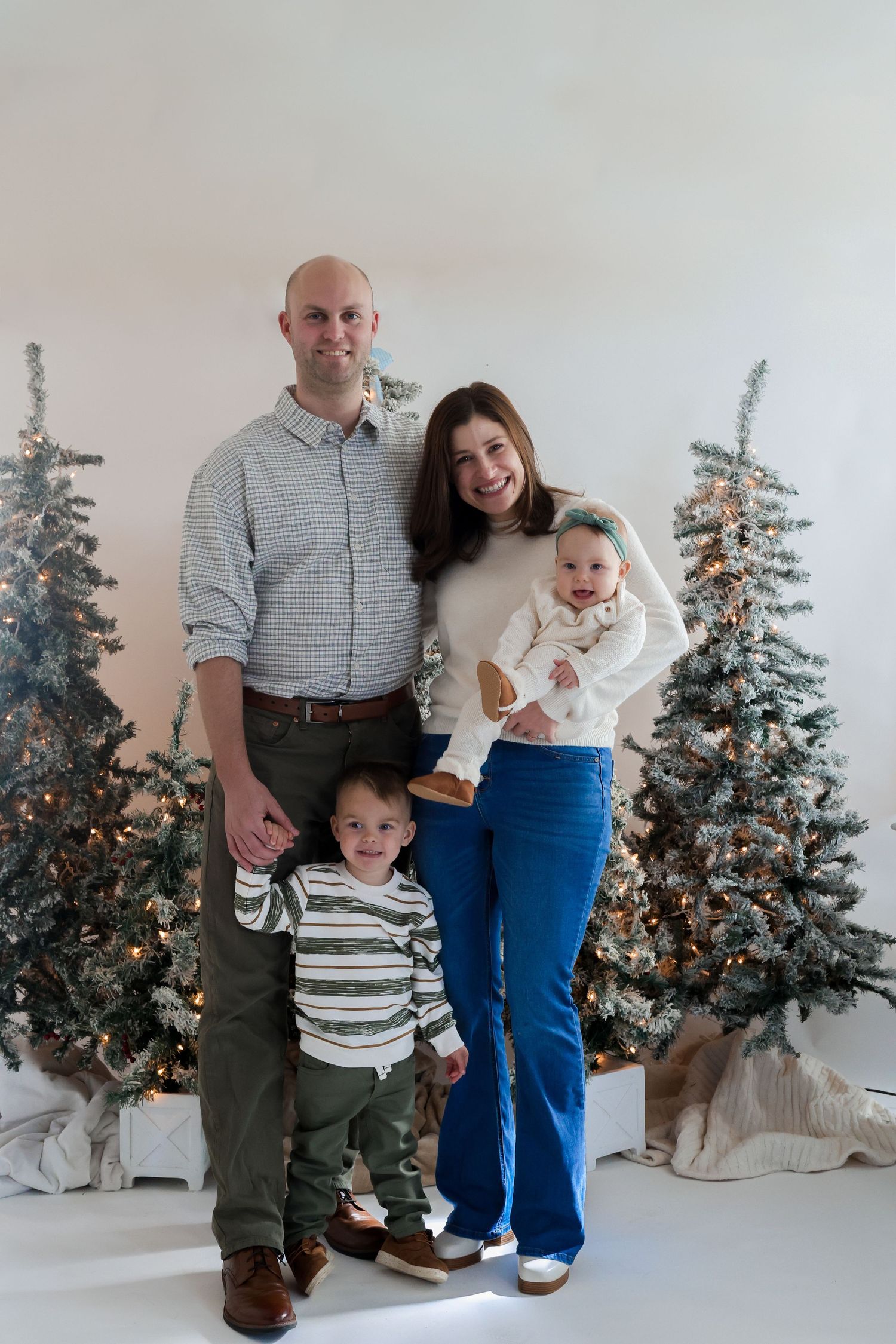 Family portrait session with Christmas trees and white decorations in the background.