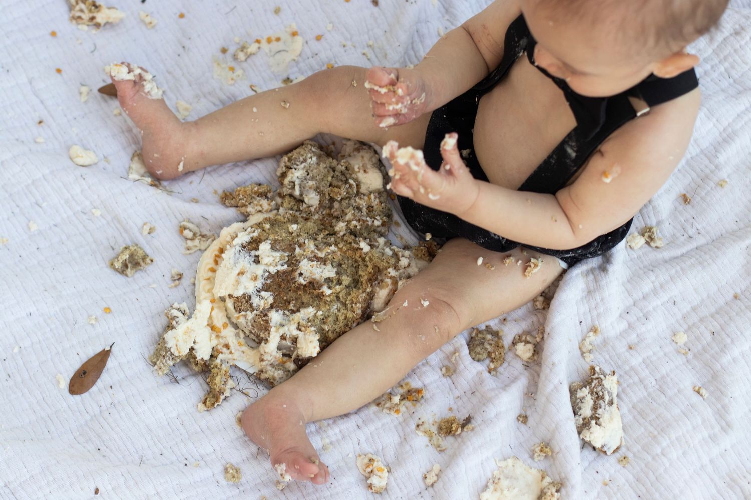 Close-up of cake smash aftermath with gold sprinkles on white blanket.