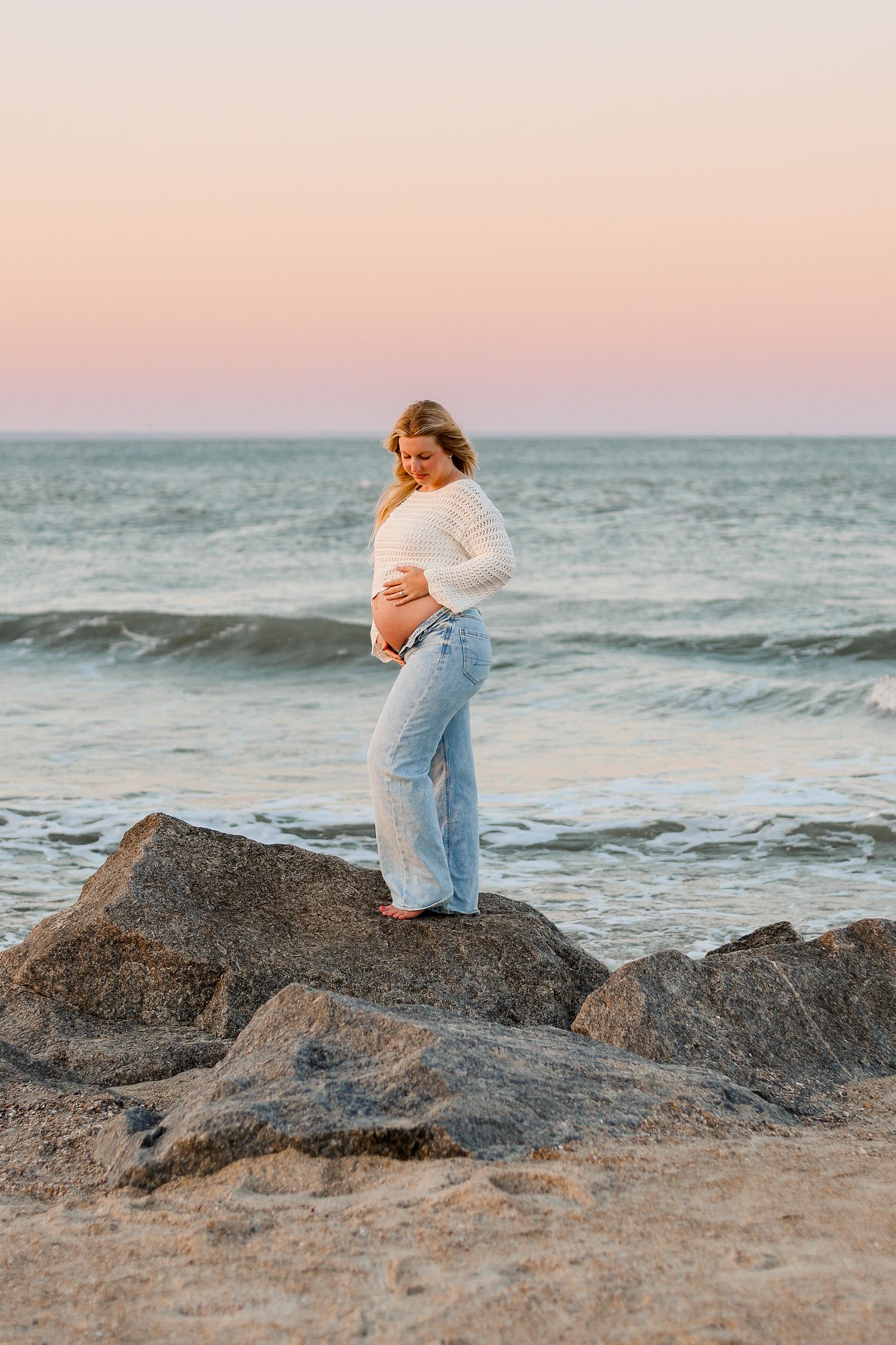 A maternity photoshoot on rocky coastal formations during sunset.