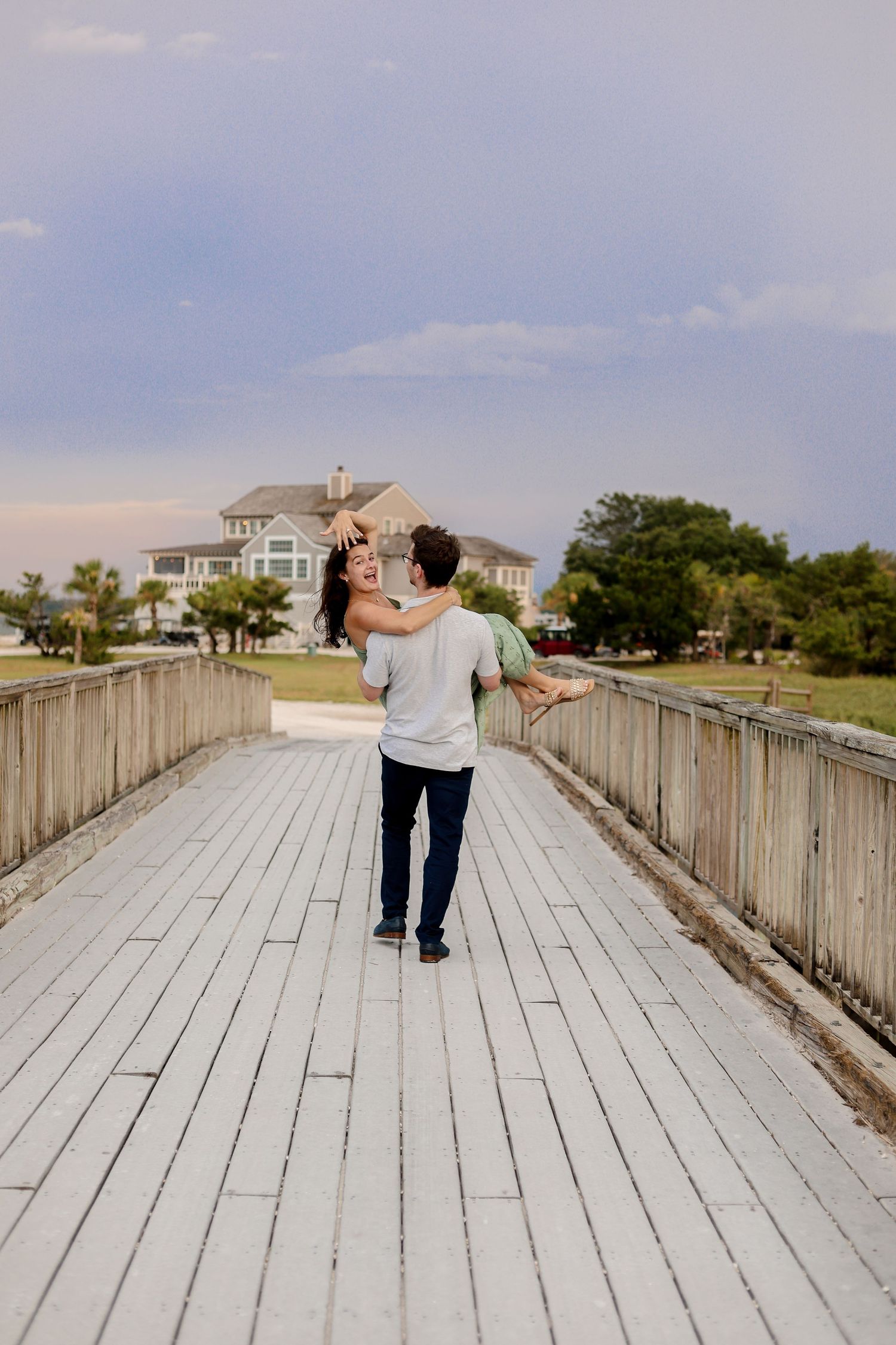 Person walking along a weathered wooden boardwalk leading to coastal beach houses on a cloudy day.