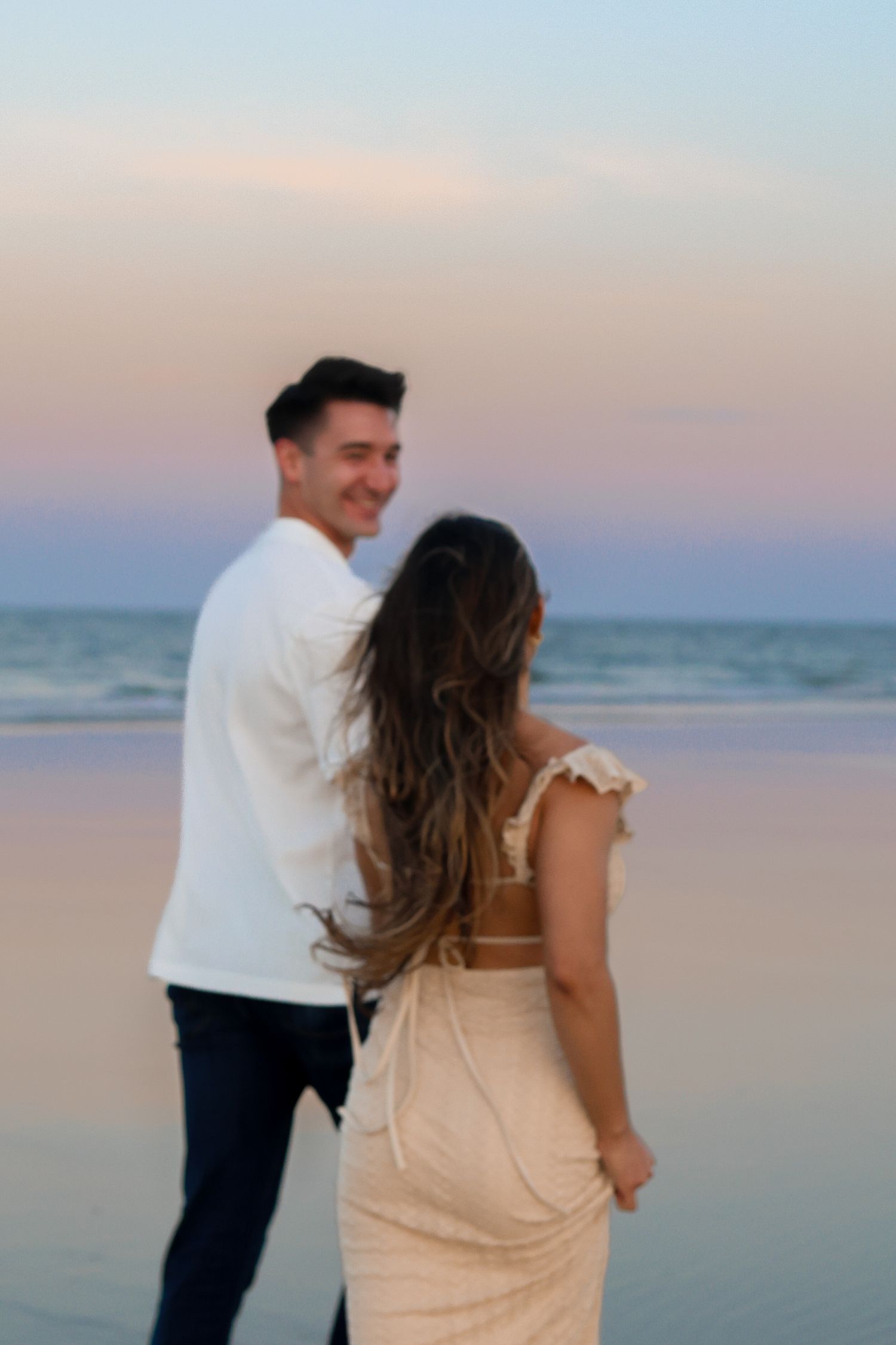 Couple sharing intimate moment on beach at dusk with ocean waves in background.