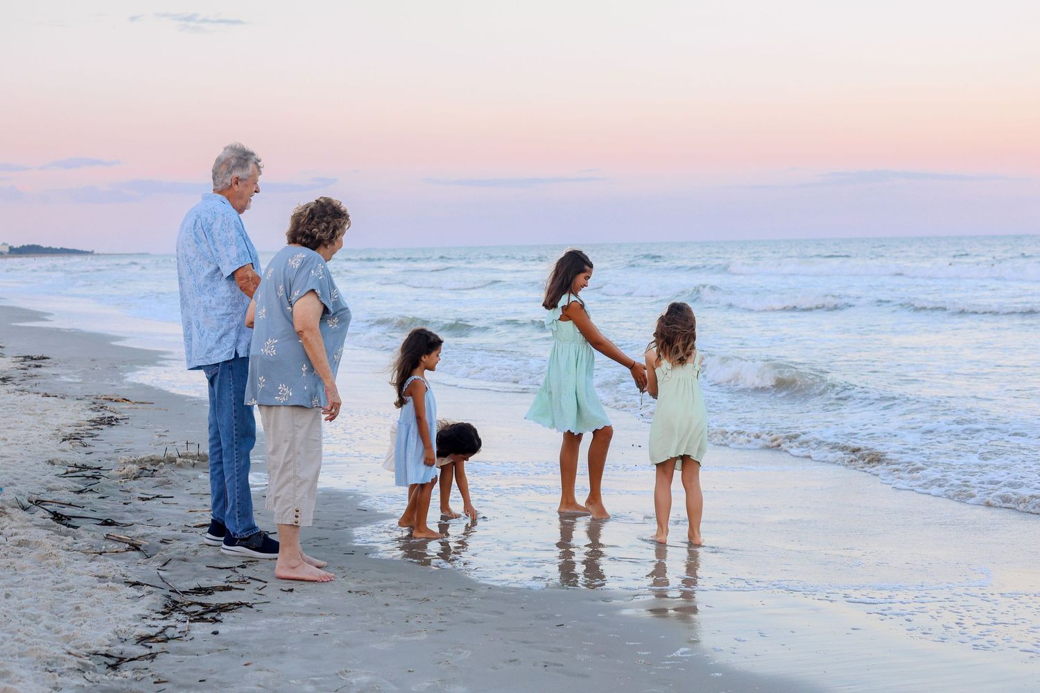 A family walks along the shoreline at sunset collecting seashells as waves crash on the beach.
