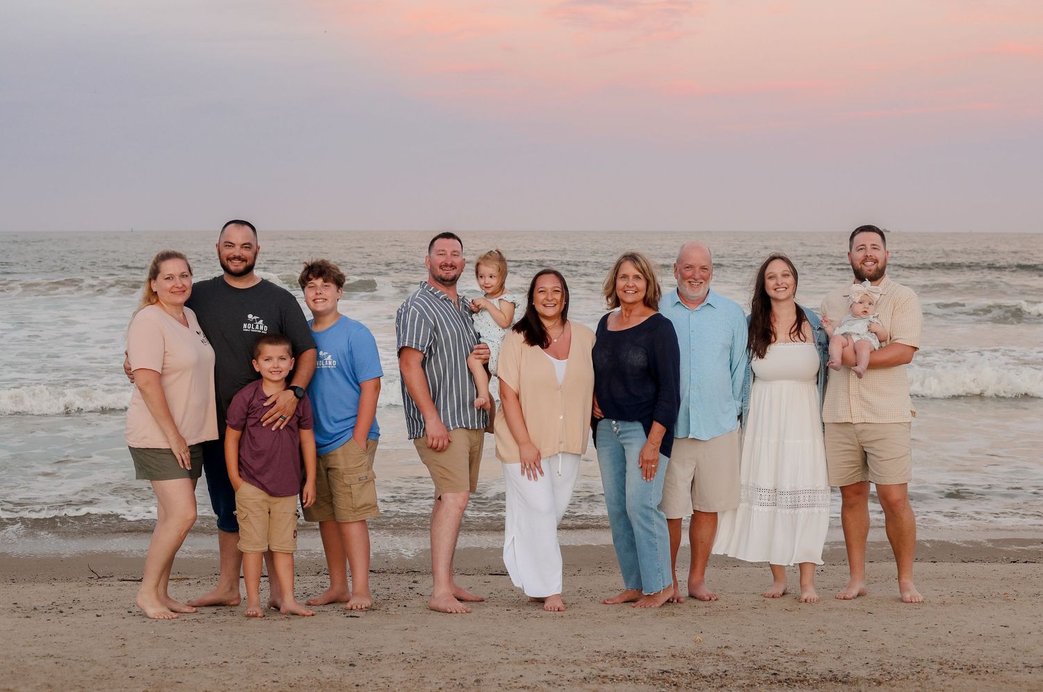 A group of people in coordinated beachwear standing together at sunset along the ocean shoreline.