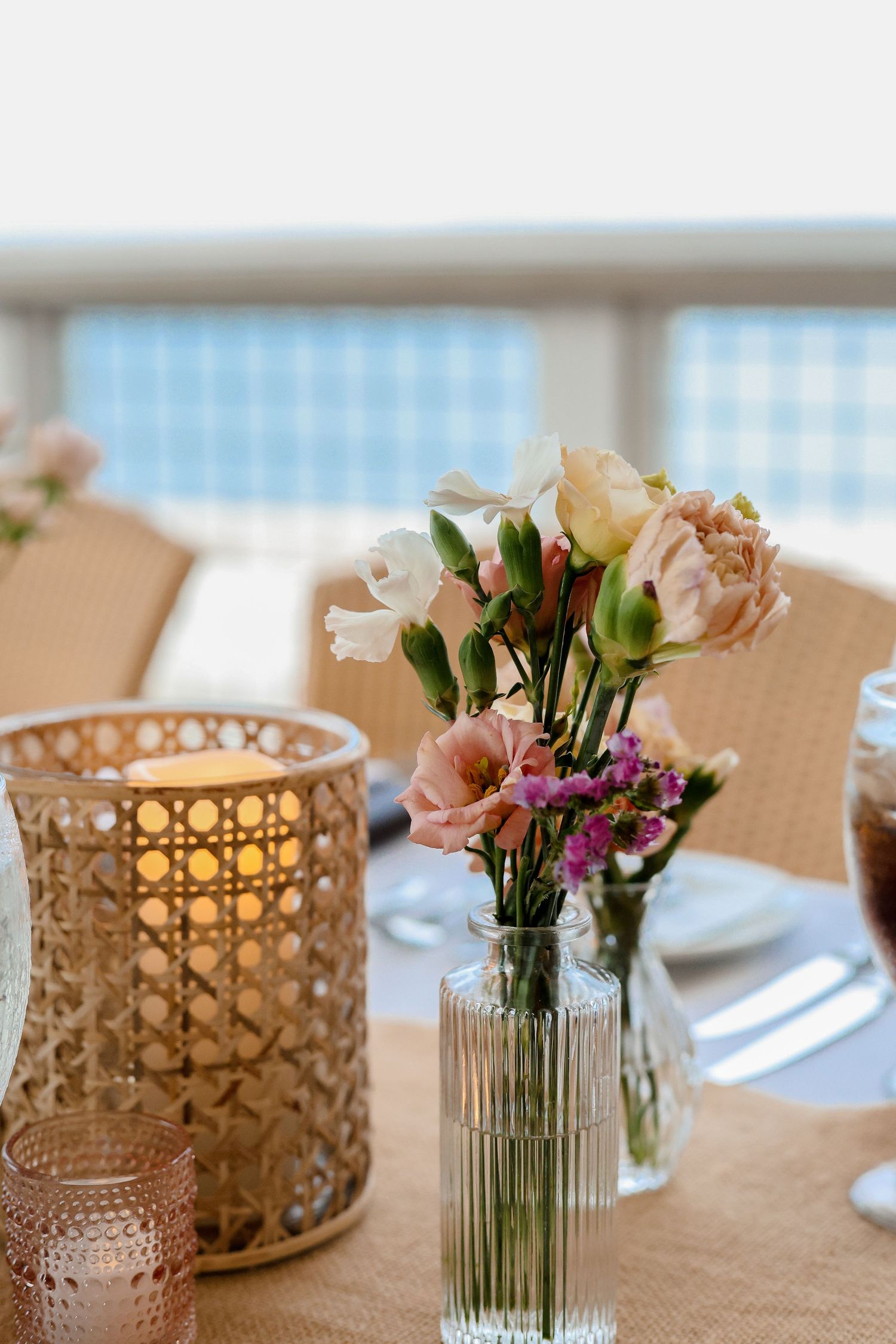 Elegant table setting with pink flowers in glass vases and gold geometric candle holders on a beige tablecloth.