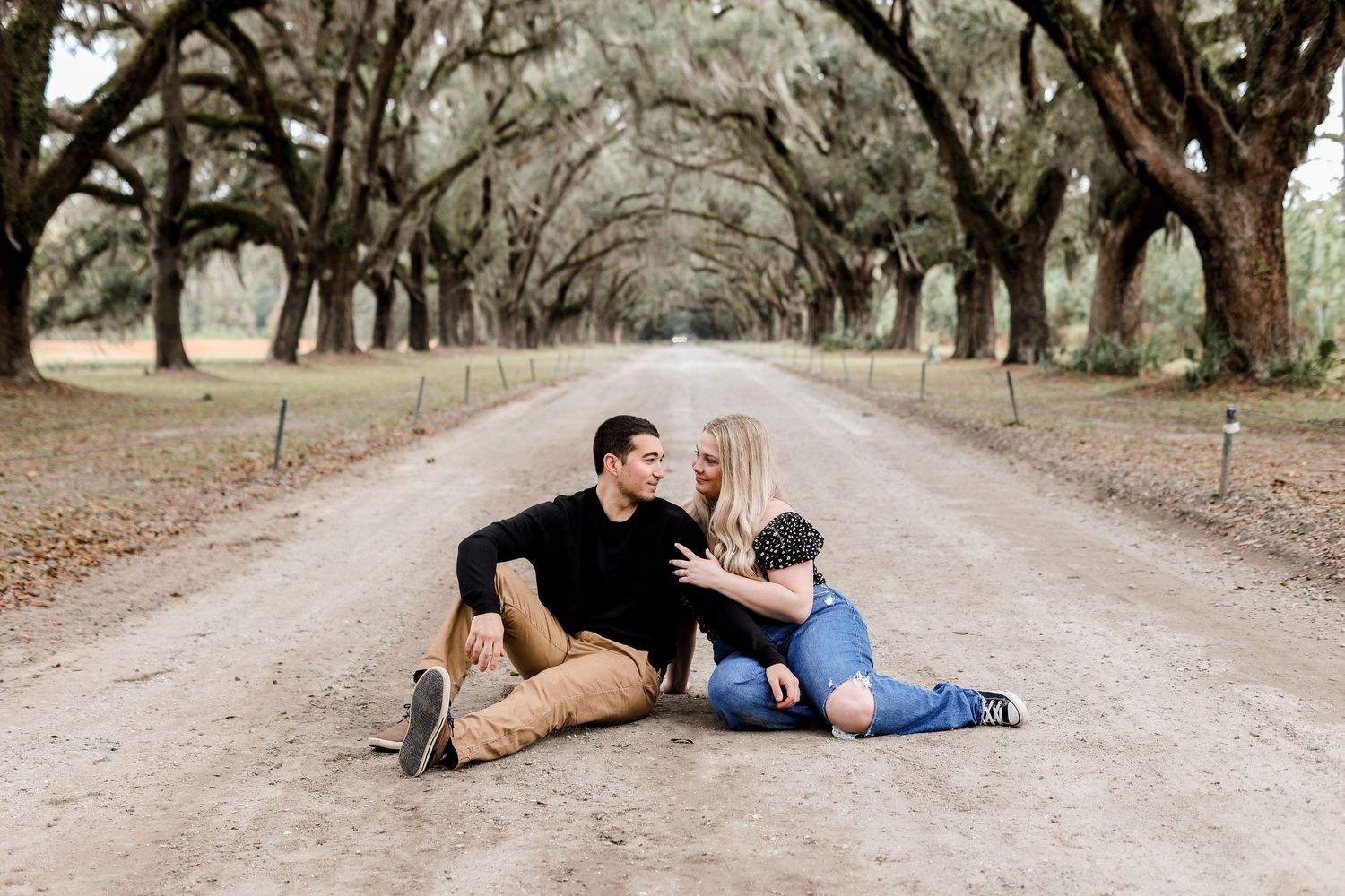 A couple sits together on a tree-lined dirt road.