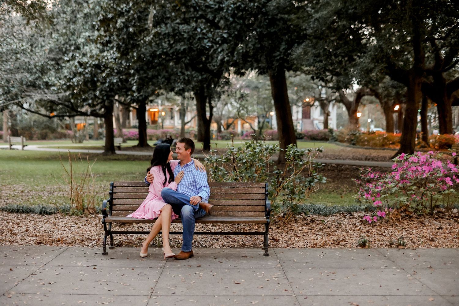 Couple sitting together on park bench surrounded by trees and autumn leaves.