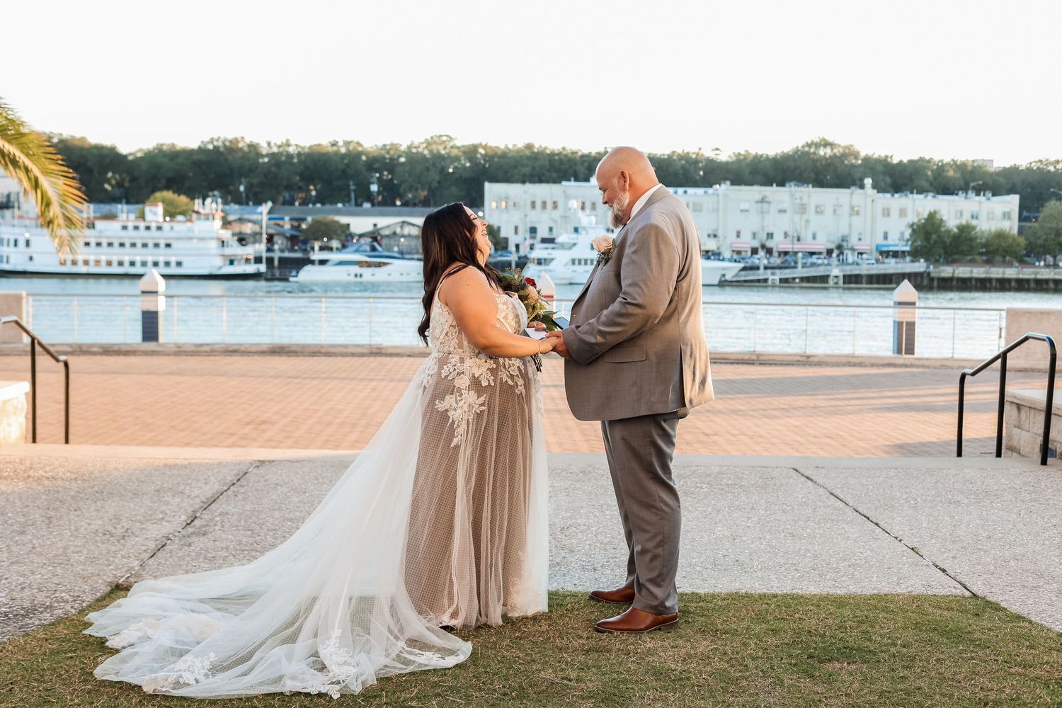 A couple shares a tender moment by the waterfront during their wedding ceremony at sunset.