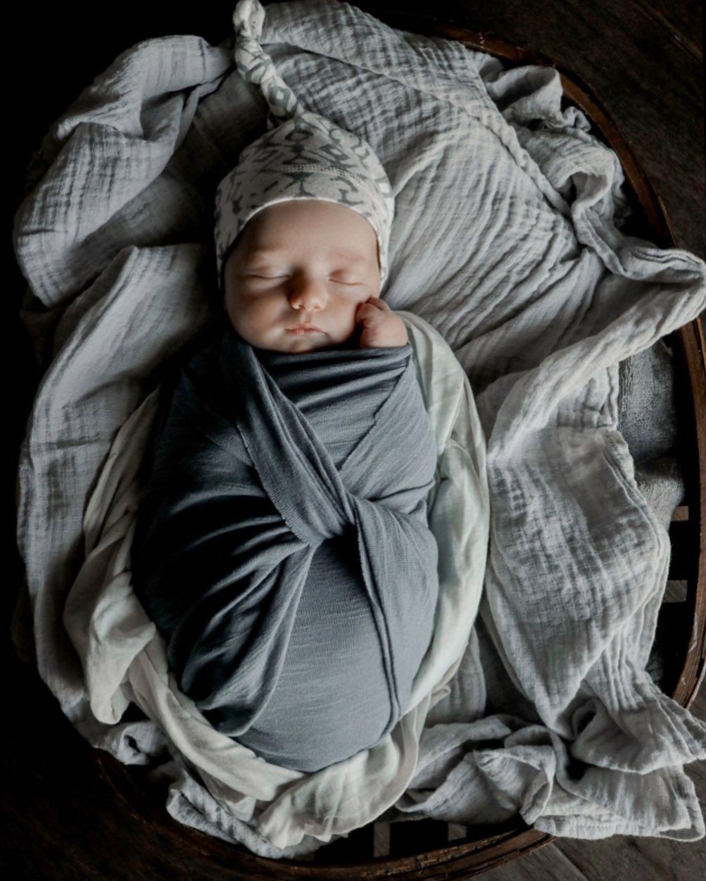 Peaceful sleeping newborn swaddled in soft gray fabric against textured white blankets.