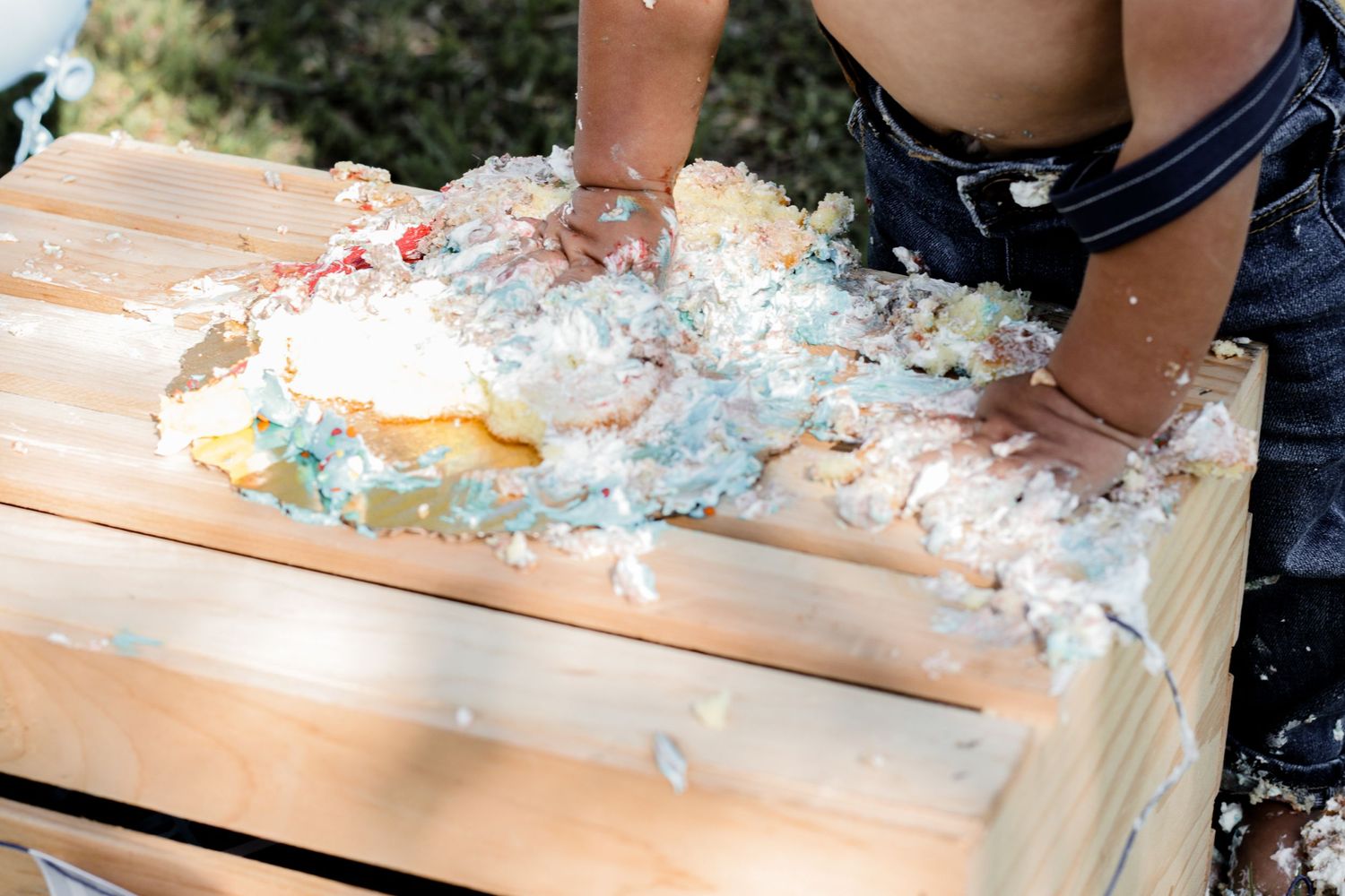 Close-up of small hands playing with smashed cake and frosting on wooden surface.