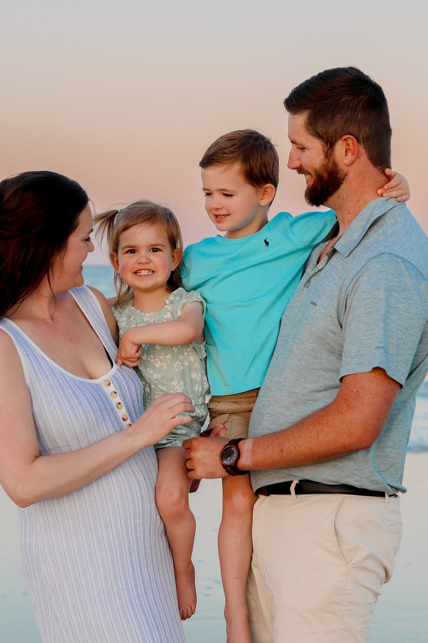 Tender family portrait session on beach at sunset in coordinated beach attire.