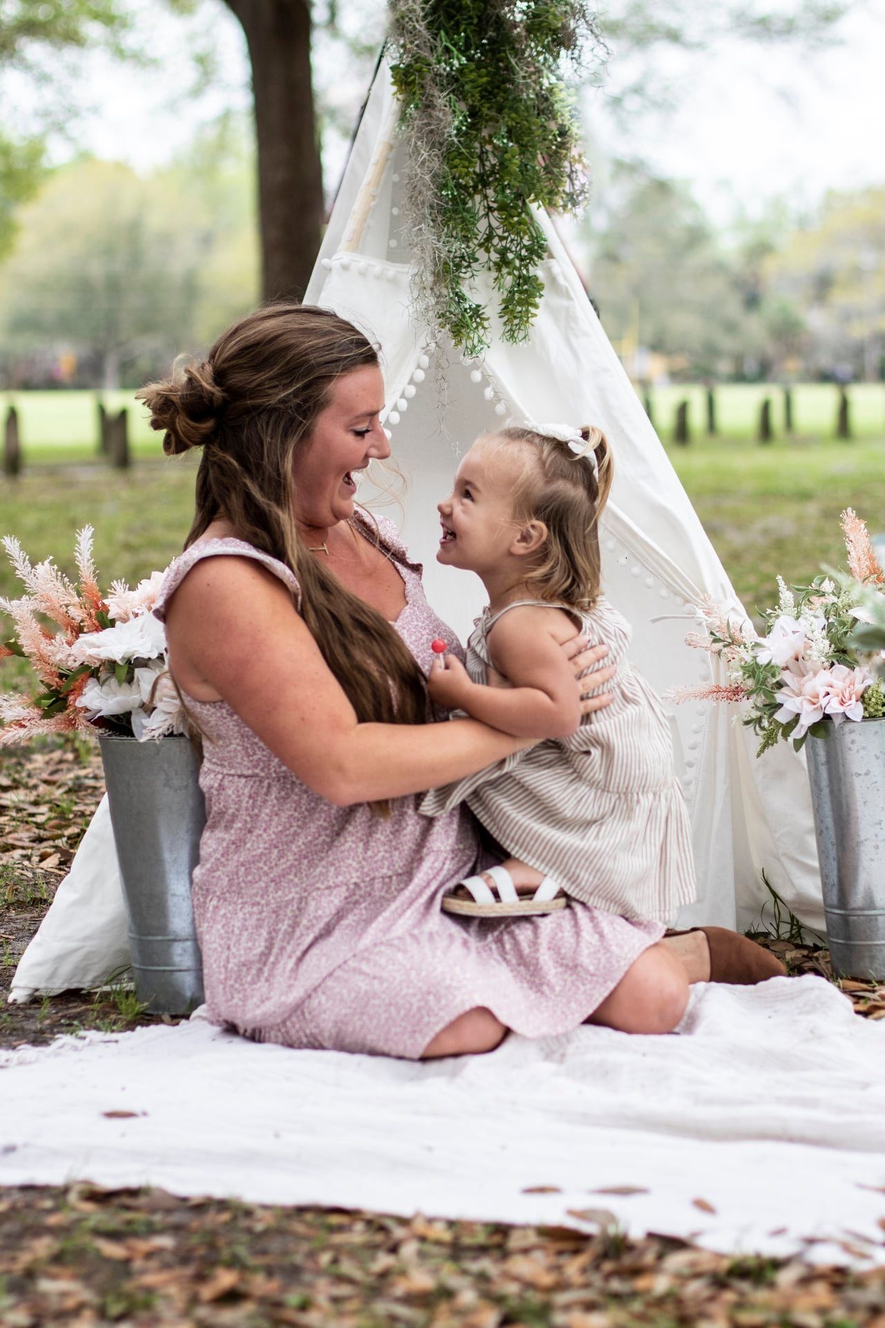 A casual photoshoot setup outdoors with white teepee tent and floral decorations.