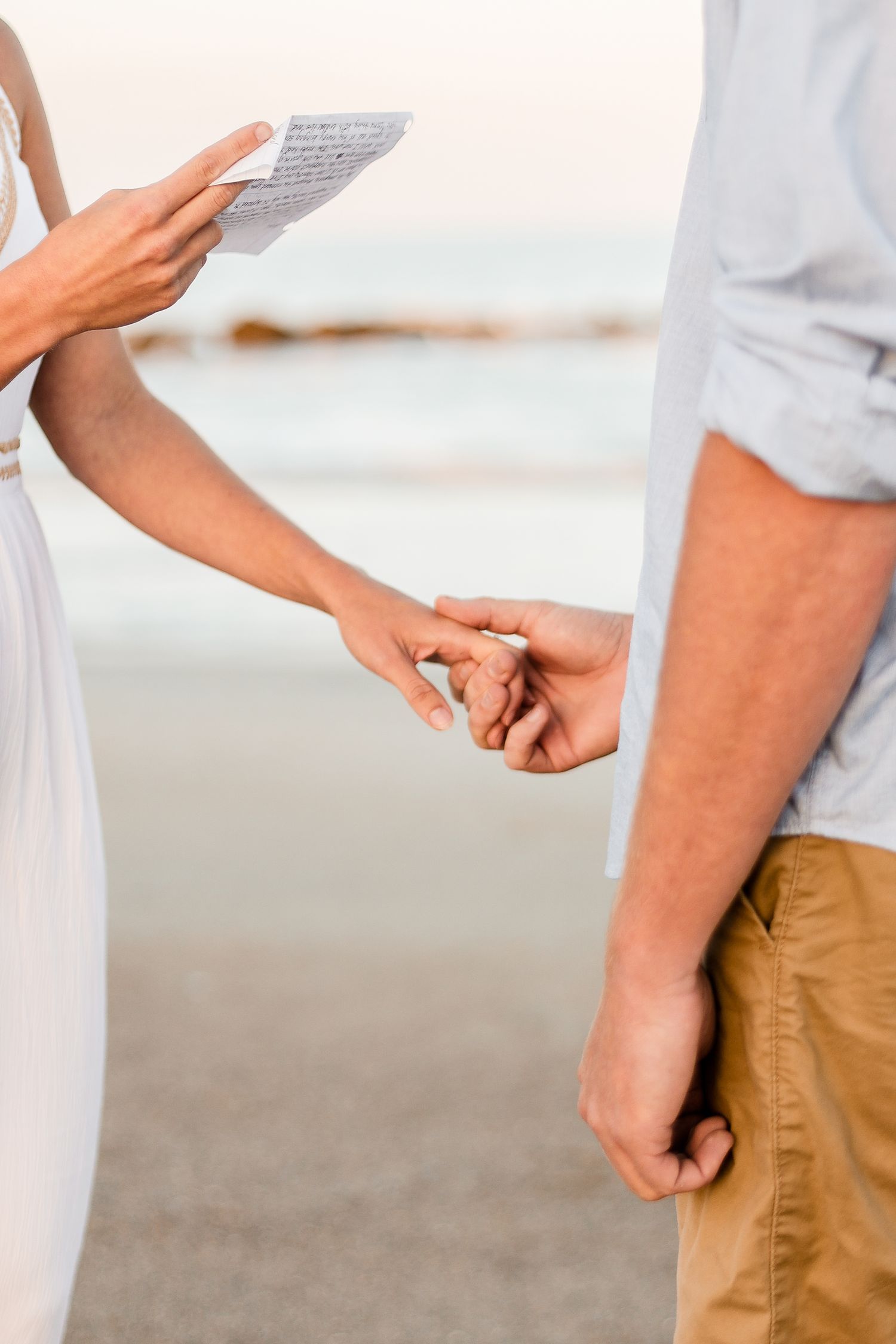 A close-up of hands holding a letter during a beachside engagement moment.