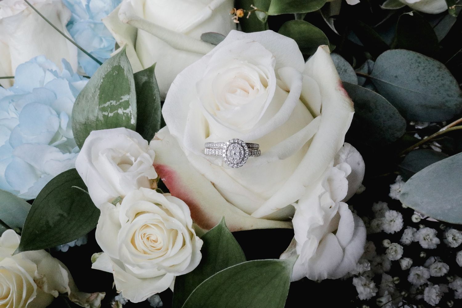 Close-up of white roses and diamond engagement ring with decorative greenery.
