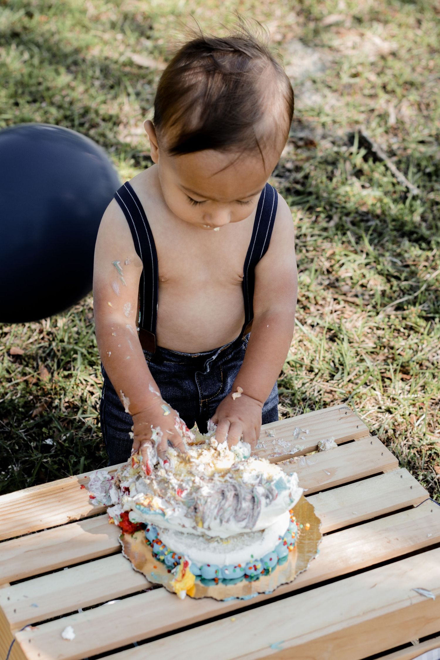Close-up of hands playing with birthday cake on wooden platform during outdoor photoshoot.