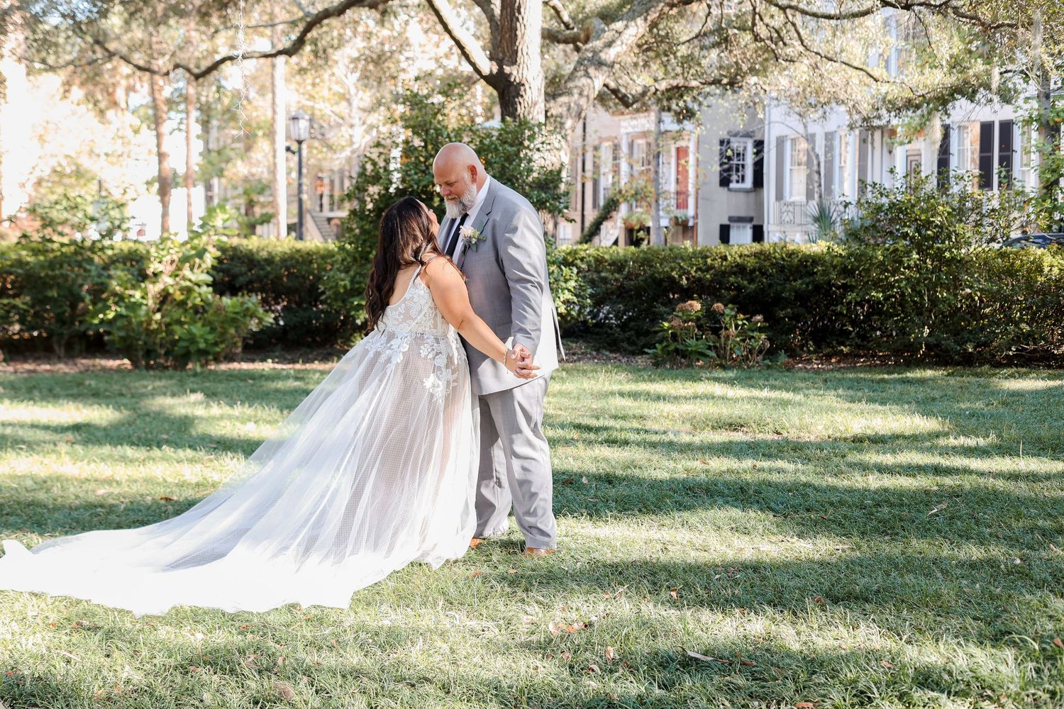 Wedding couple poses for romantic photos on a sunlit lawn with historic buildings in background.