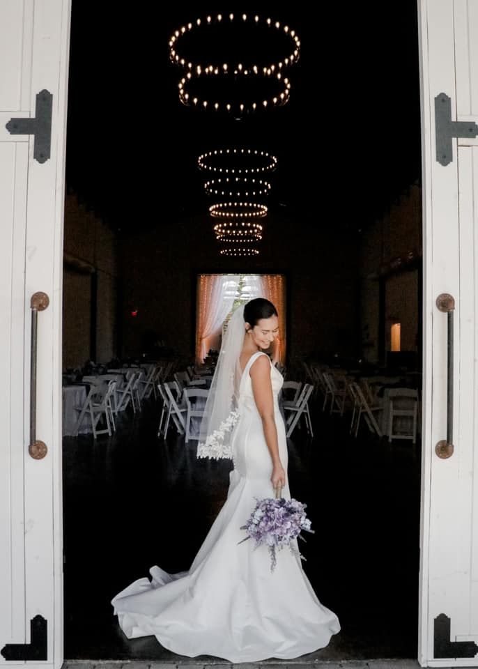 Bride in white gown under circular light fixtures in elegant venue doorway.
