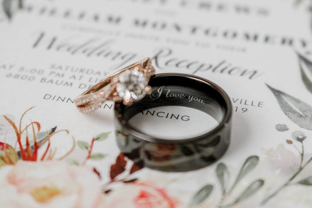 Wedding rings photographed on floral invitation with rose gold and black bands.