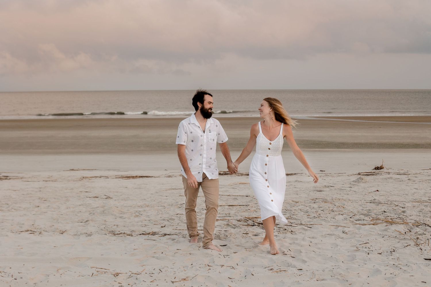 A couple walks hand in hand on a beach at sunset.