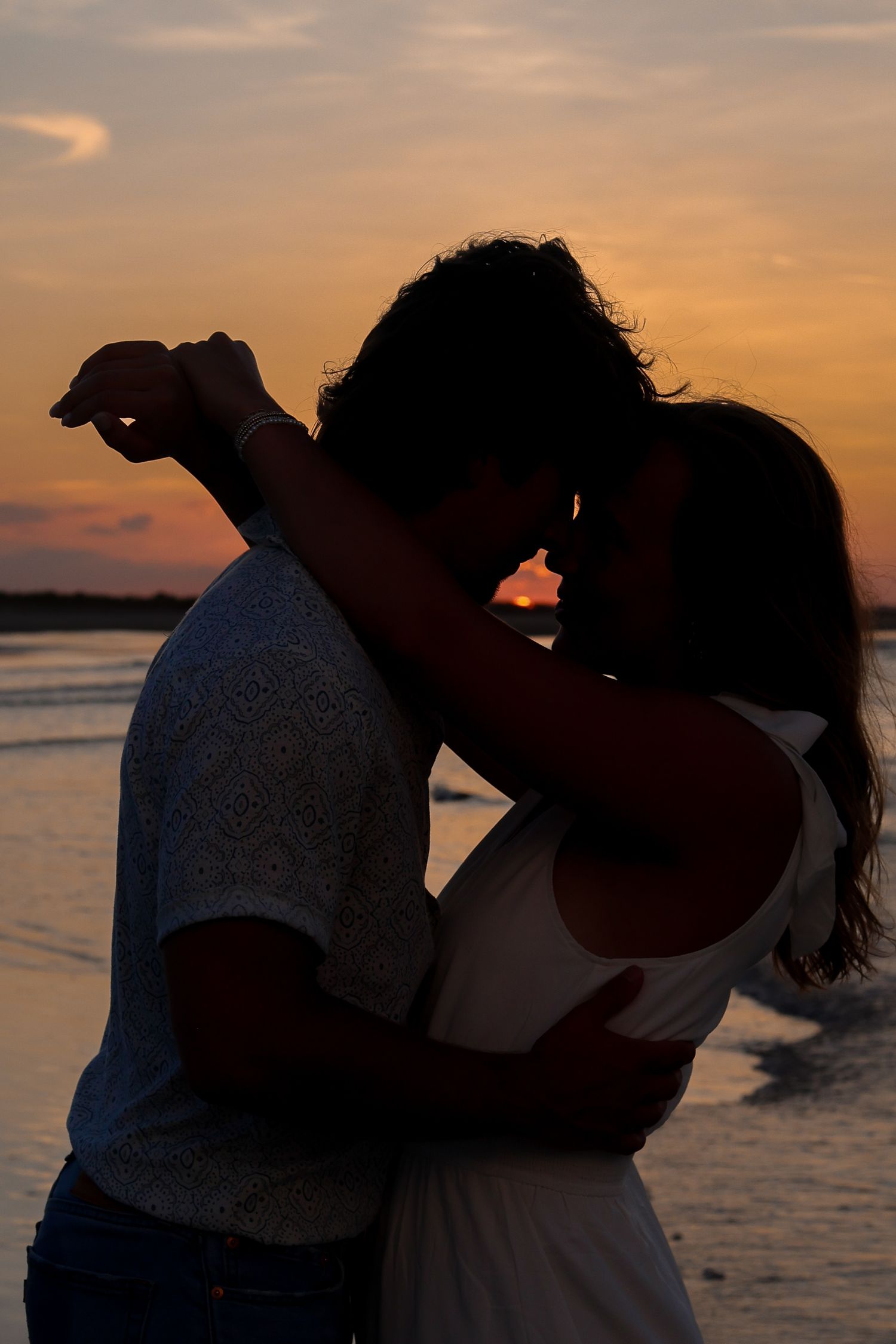 Silhouetted couple sharing an intimate embrace on the beach during golden hour.