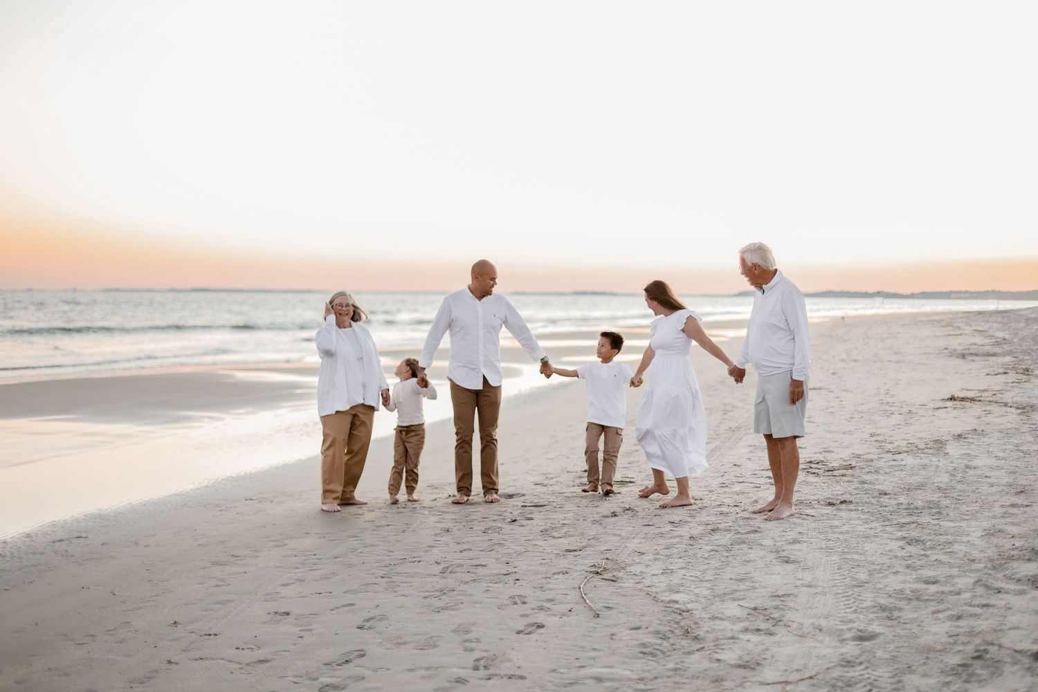 Group of people in white outfits walking along a beach at sunset.