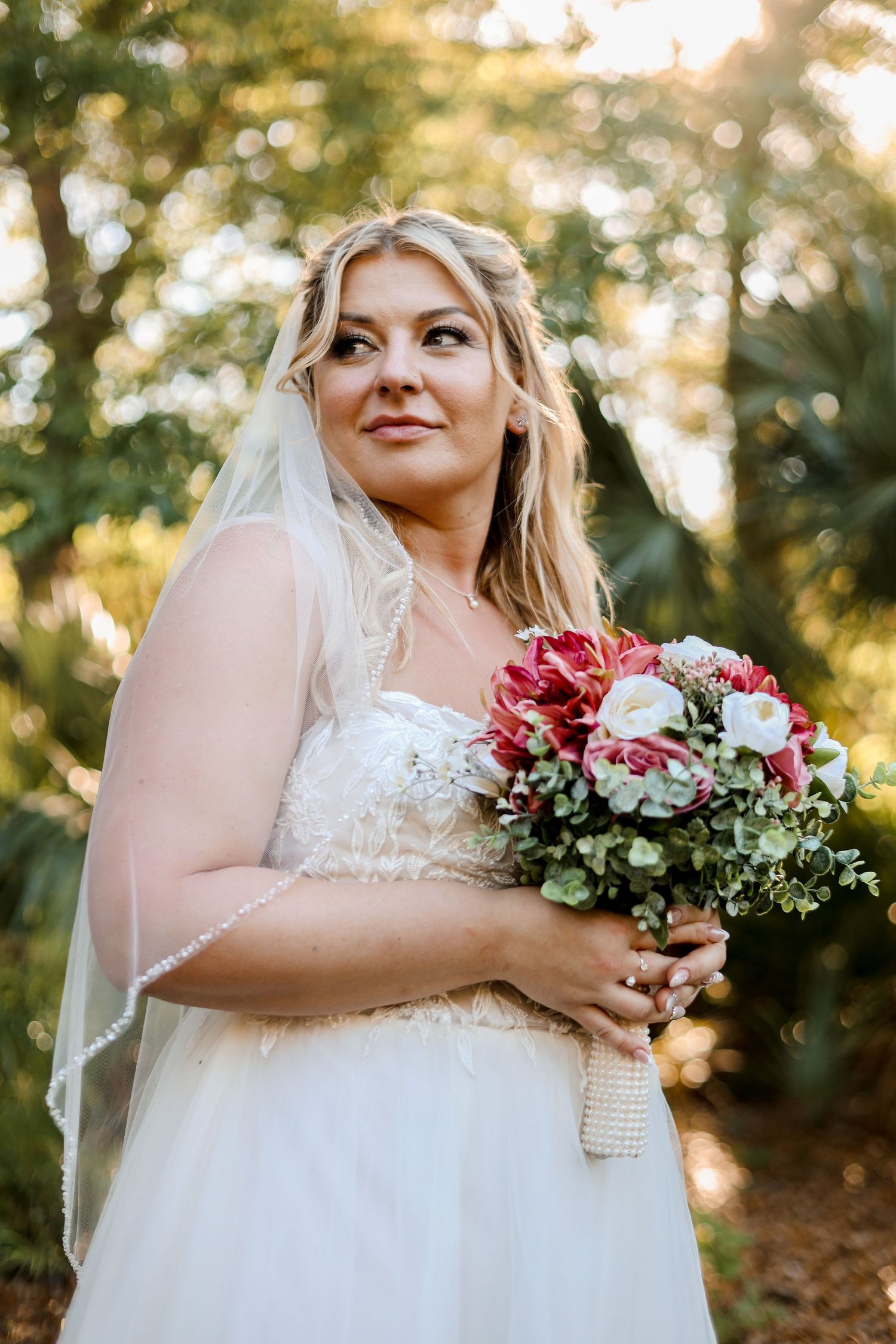 Bride holding pink and white bouquet in sunlit outdoor setting.