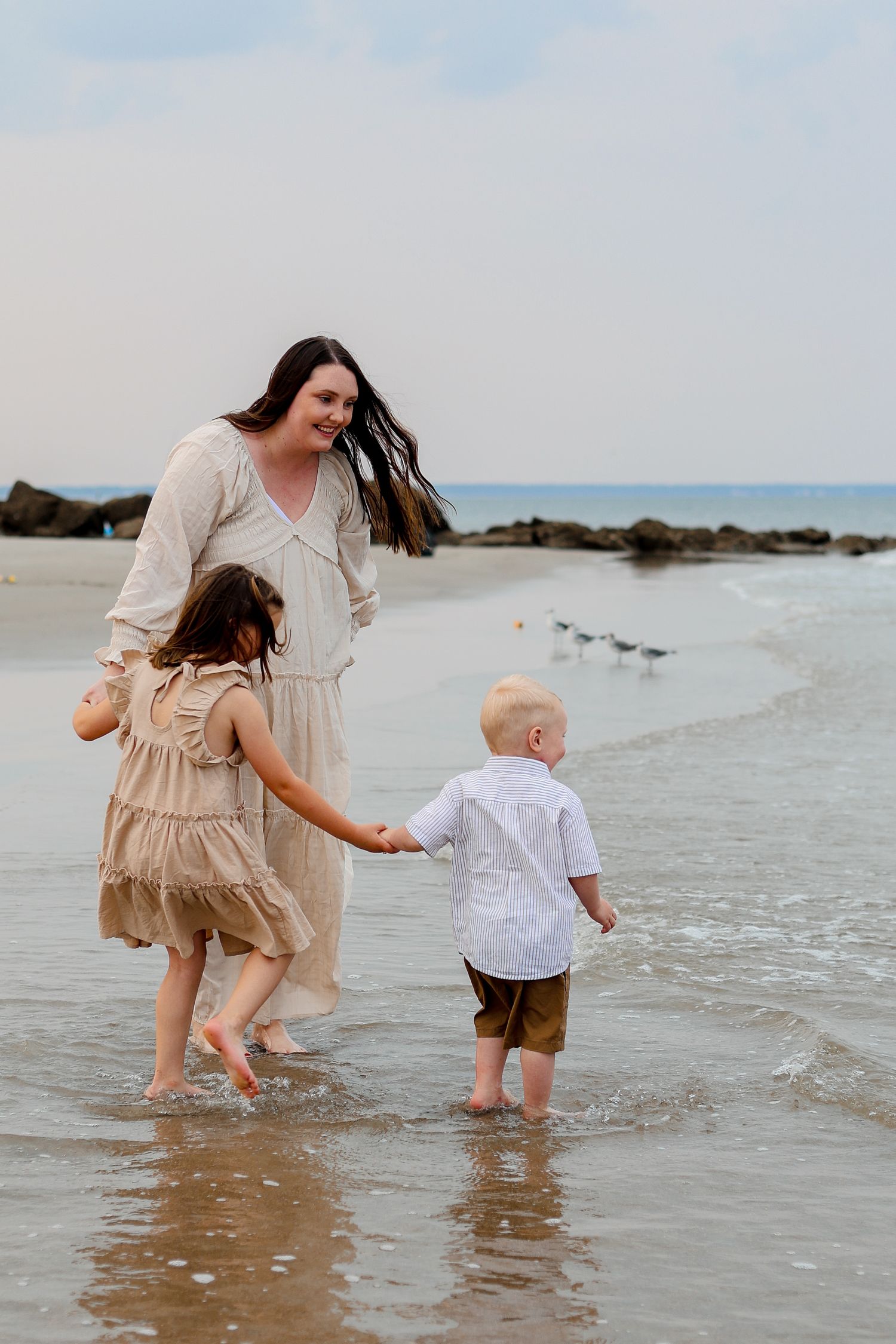 People holding hands while wading in shallow ocean water at beach.