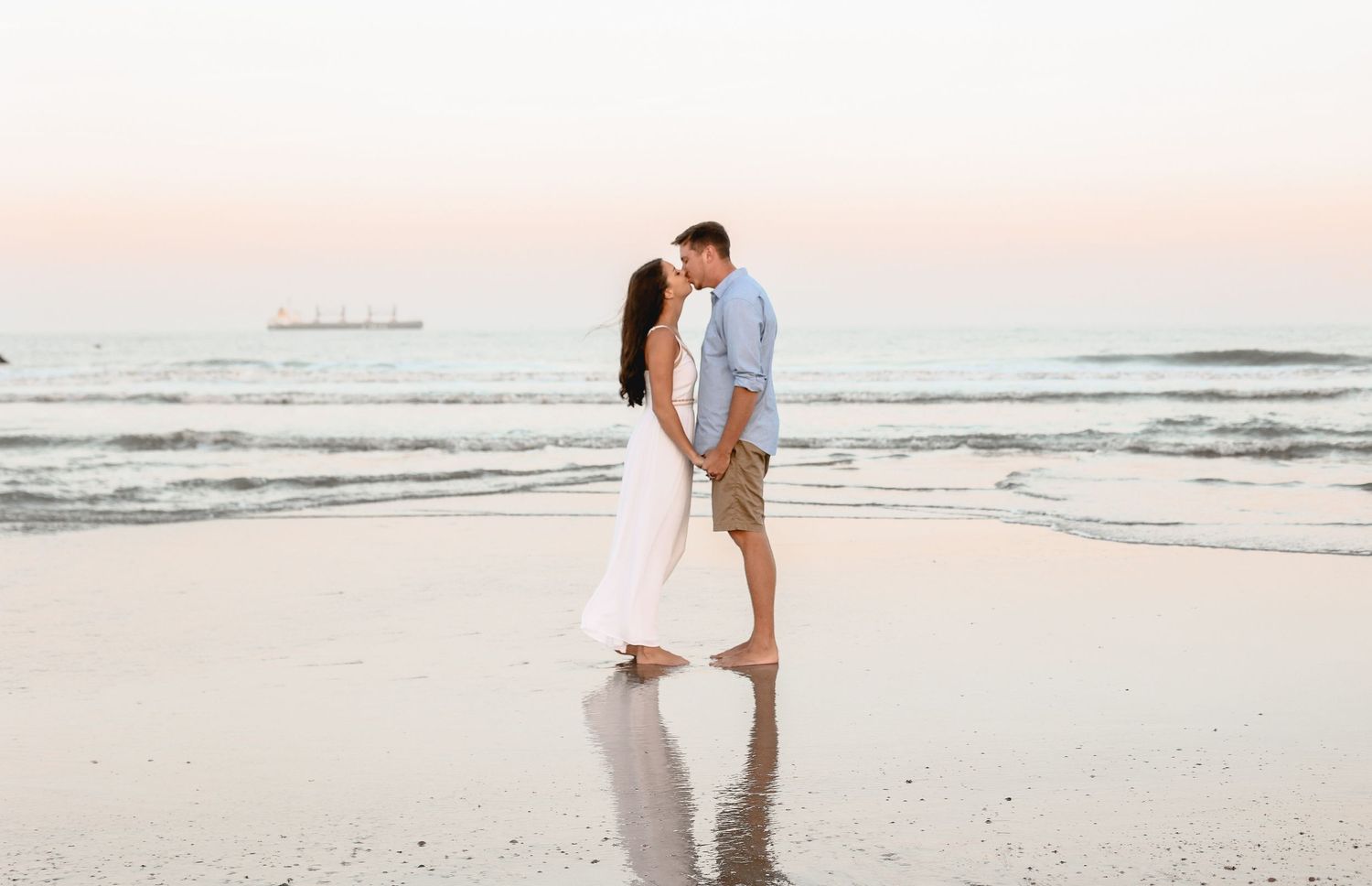 A couple embraces during sunset on a beach wearing coordinated white and blue outfits.