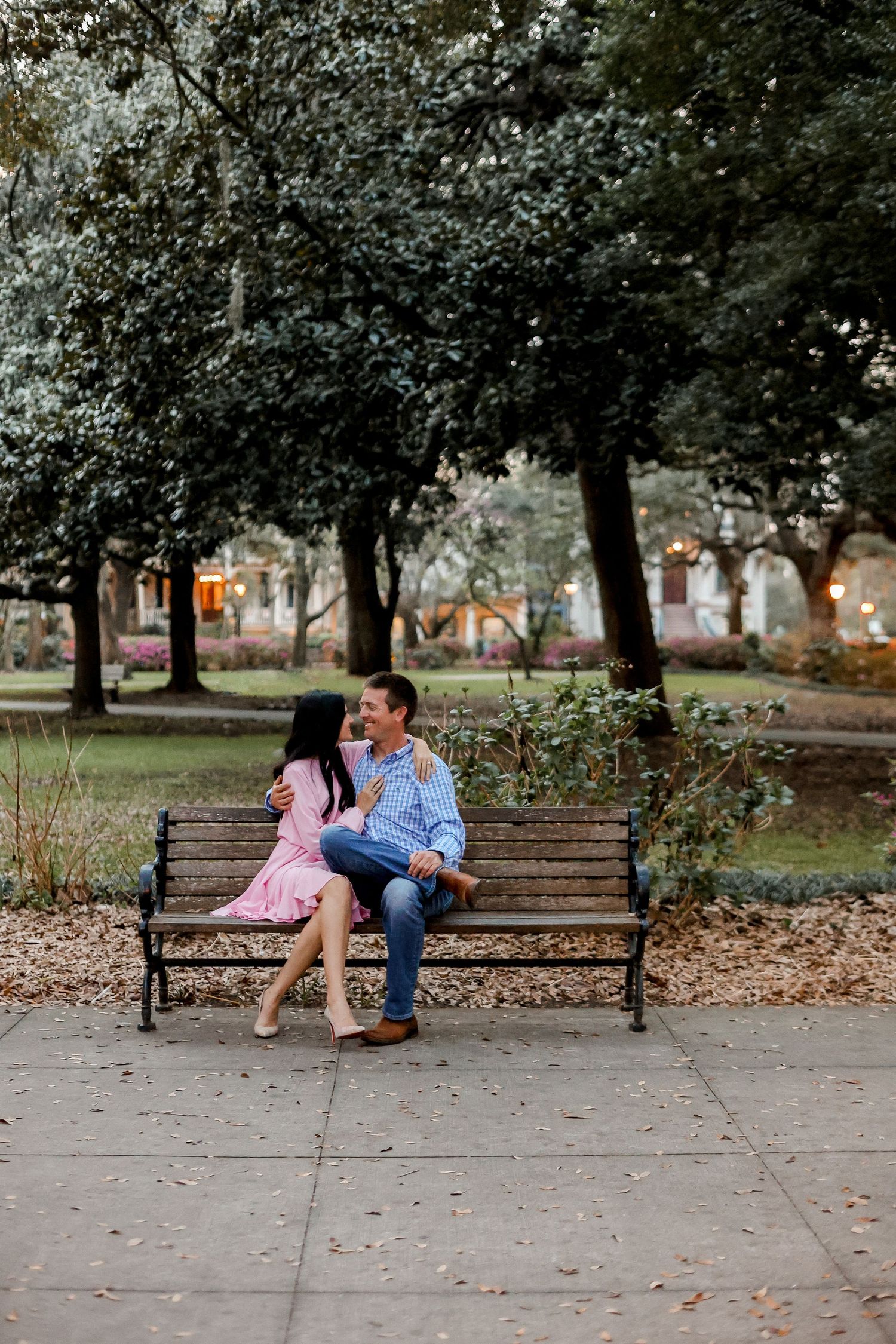 Couple sitting together on park bench surrounded by trees in autumn setting.