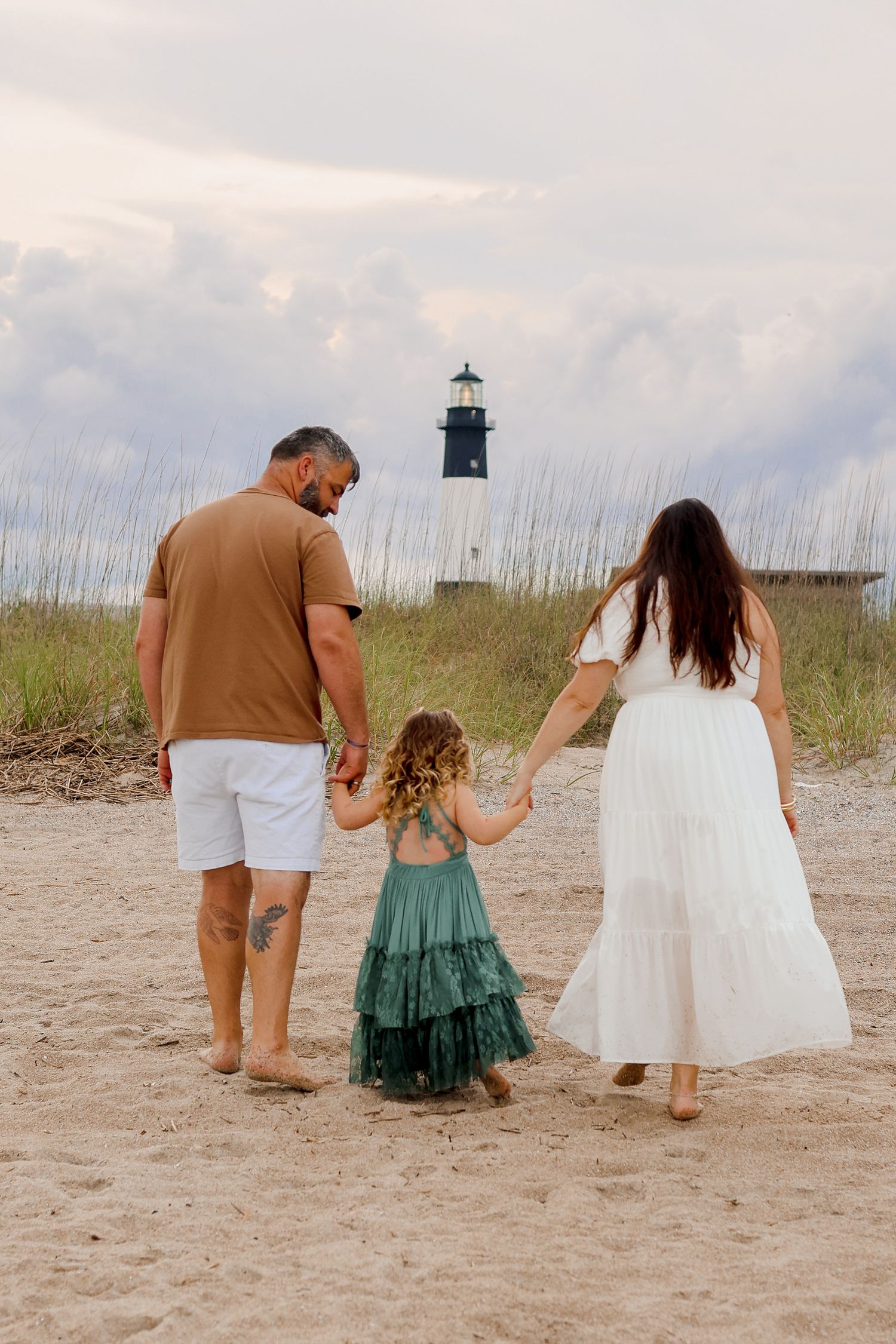 Family exploring sand dunes with lighthouse in background during golden hour.