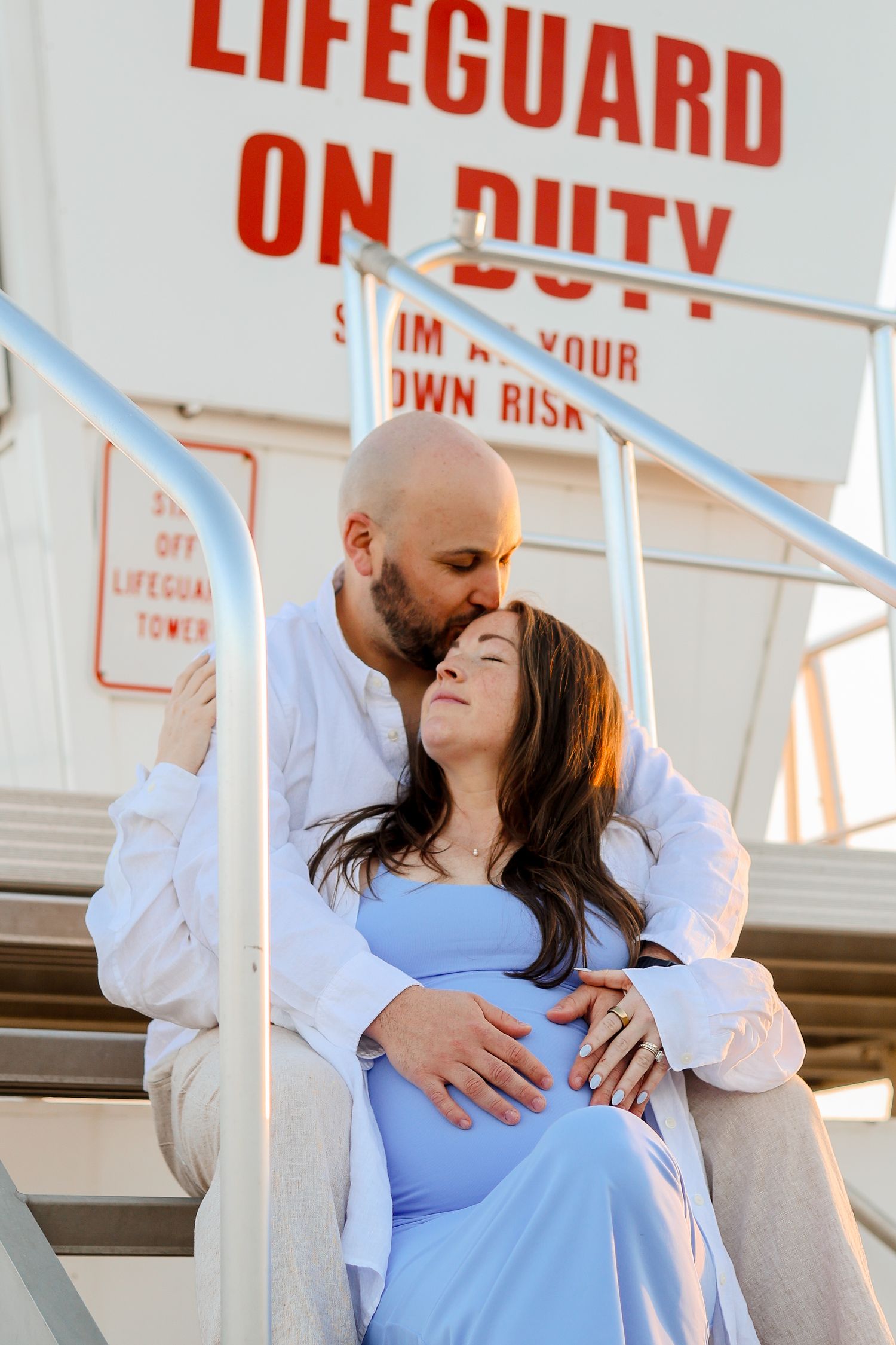 Romantic maternity photo at a lifeguard tower during sunset.