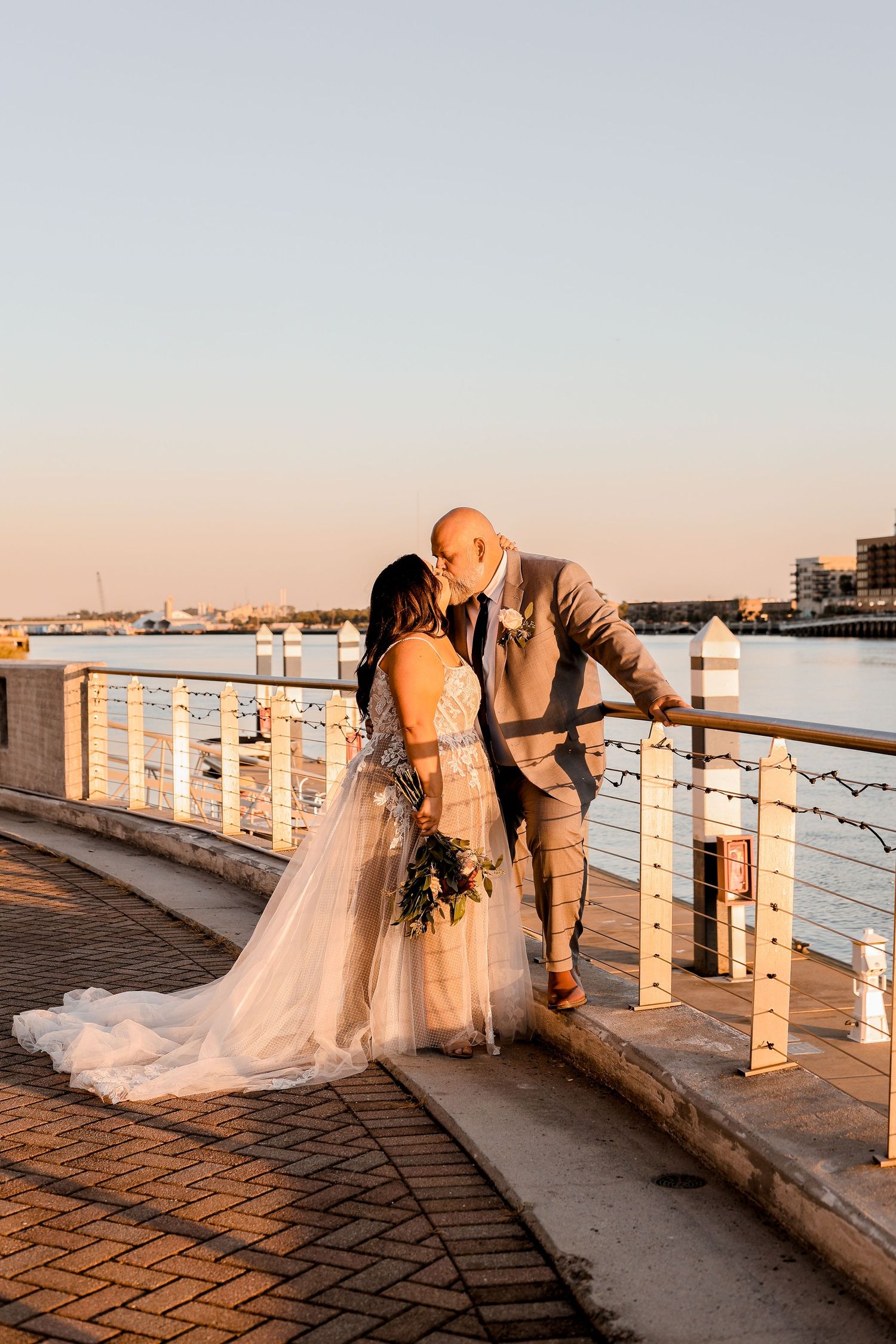 A romantic sunset wedding photo of a couple embracing on a waterfront pier.