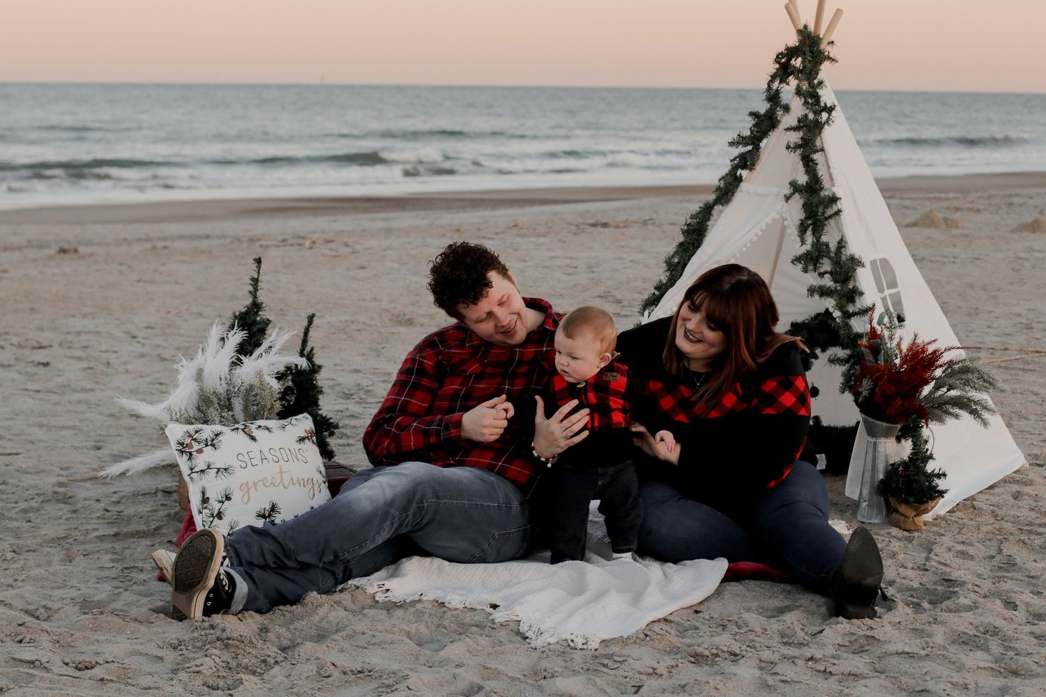 A family shares a tender moment on a beach at sunset near a decorated white tent.