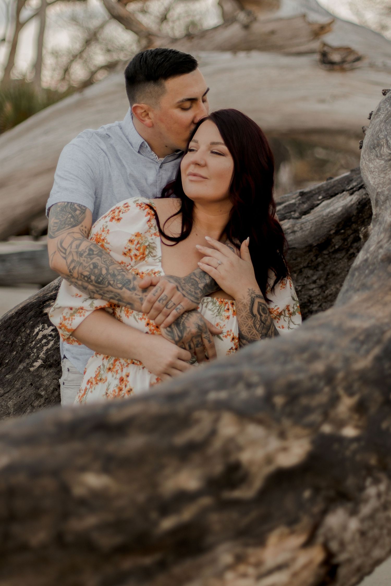 Intimate couple sharing tender moment among beach driftwood at sunset.