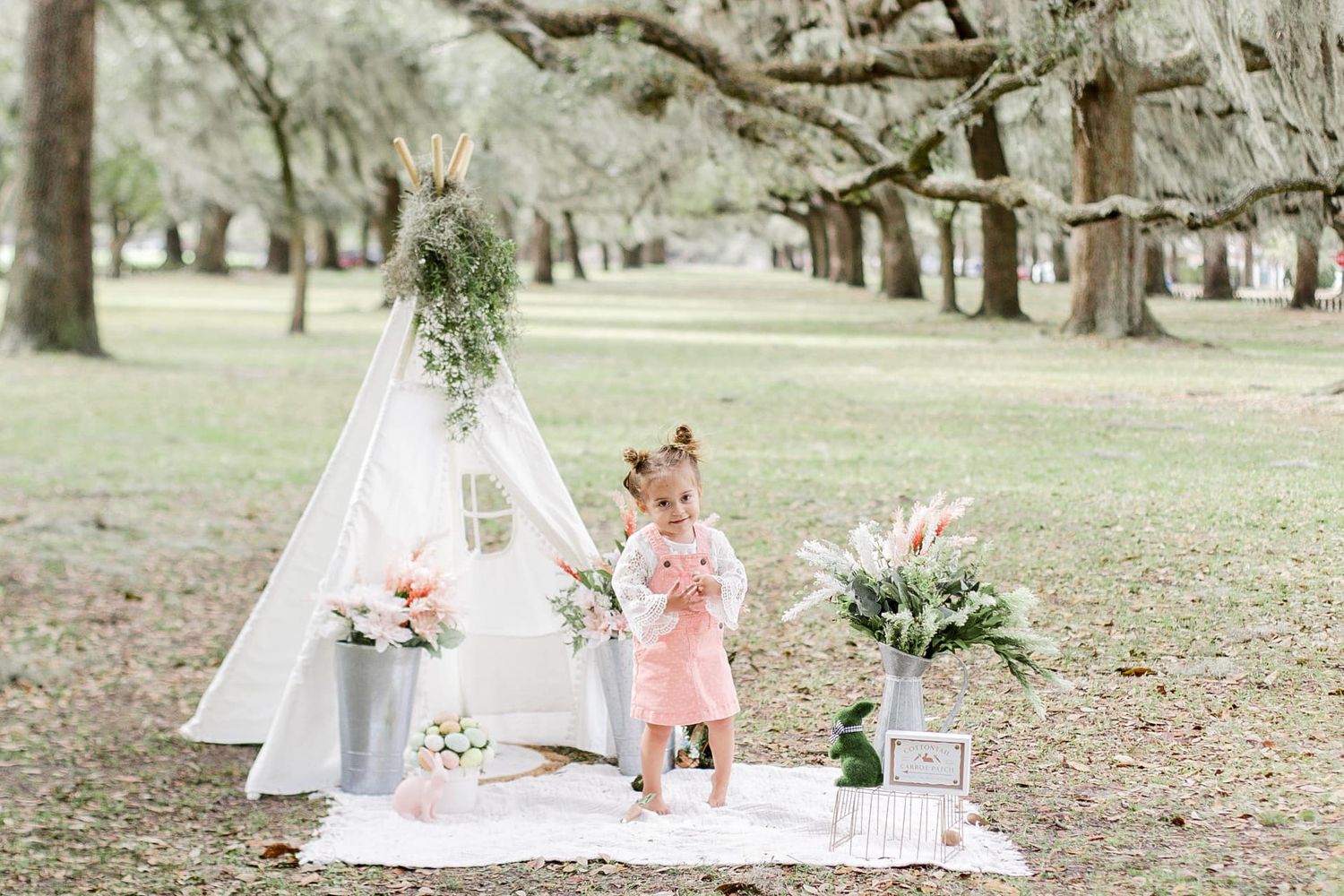 Outdoor photo setup with white teepee tent and spring decorations in a park setting.
