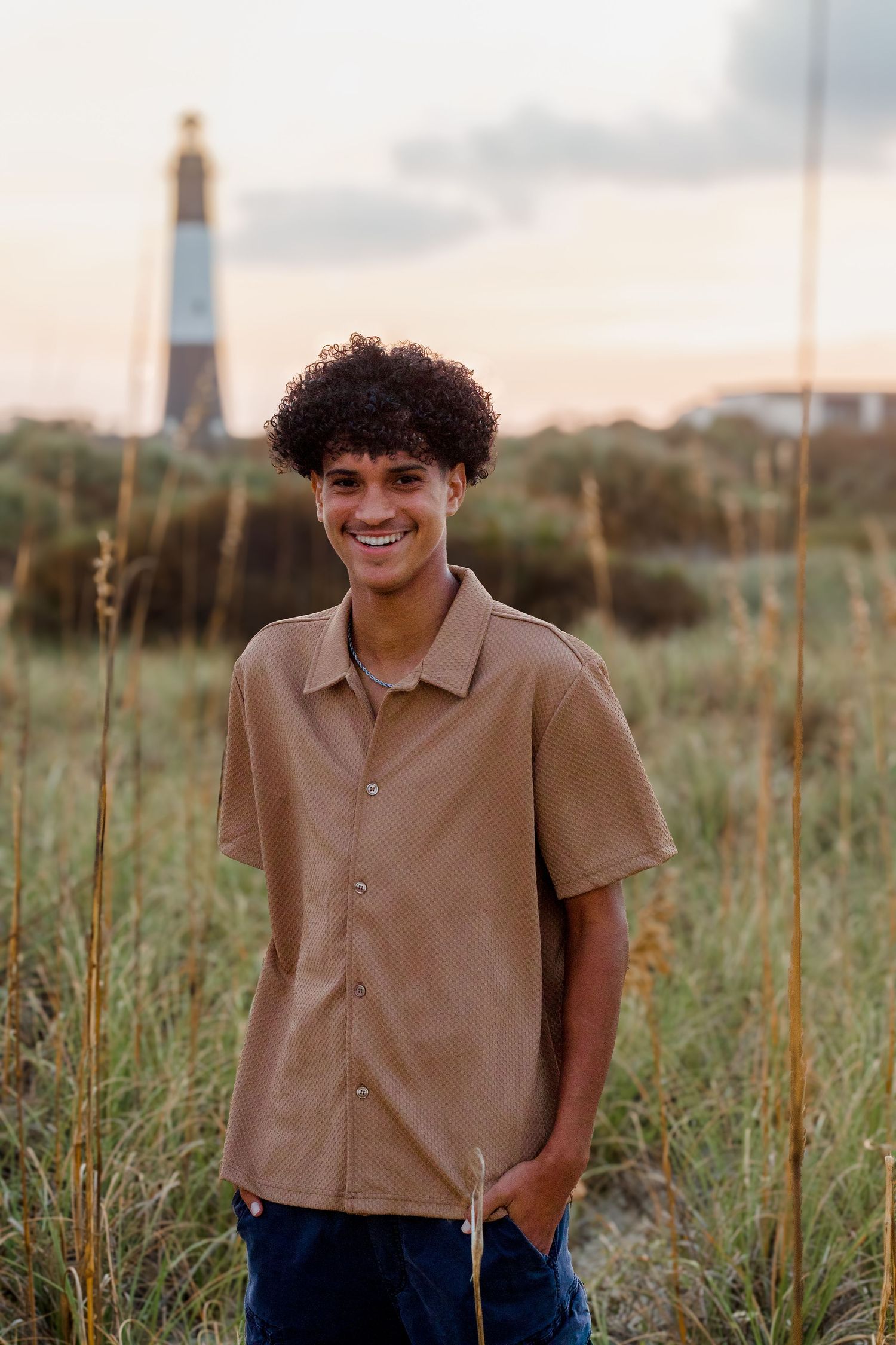 Sunset portrait in tall grass with lighthouse silhouette in background.