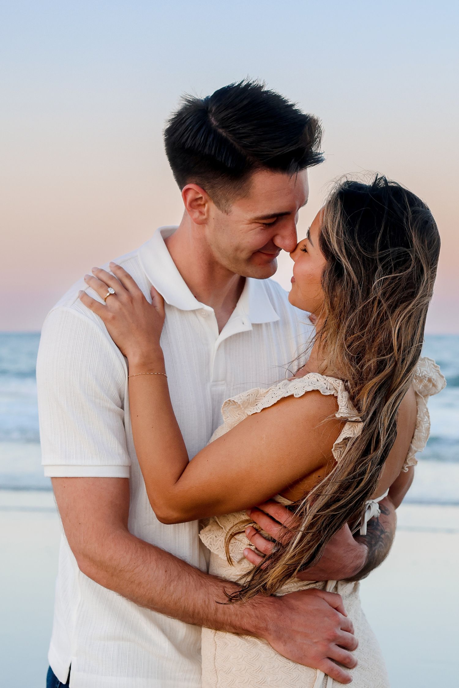 Intimate couple portrait on beach with soft sunset lighting and ocean backdrop.